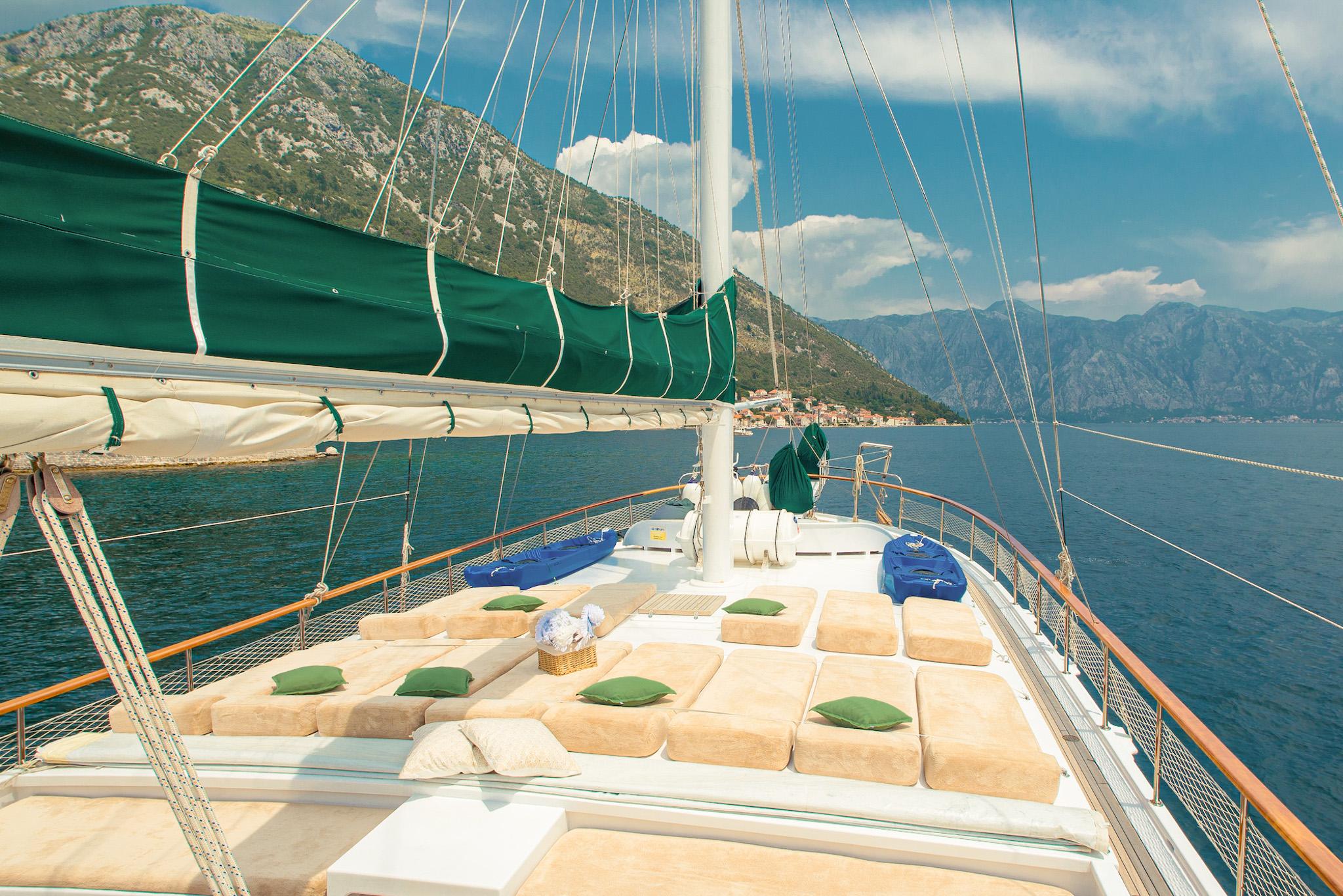Gulet bow sun deck with beige cushioned loungers and green pillows sailing Bay of Kotor Montenegro