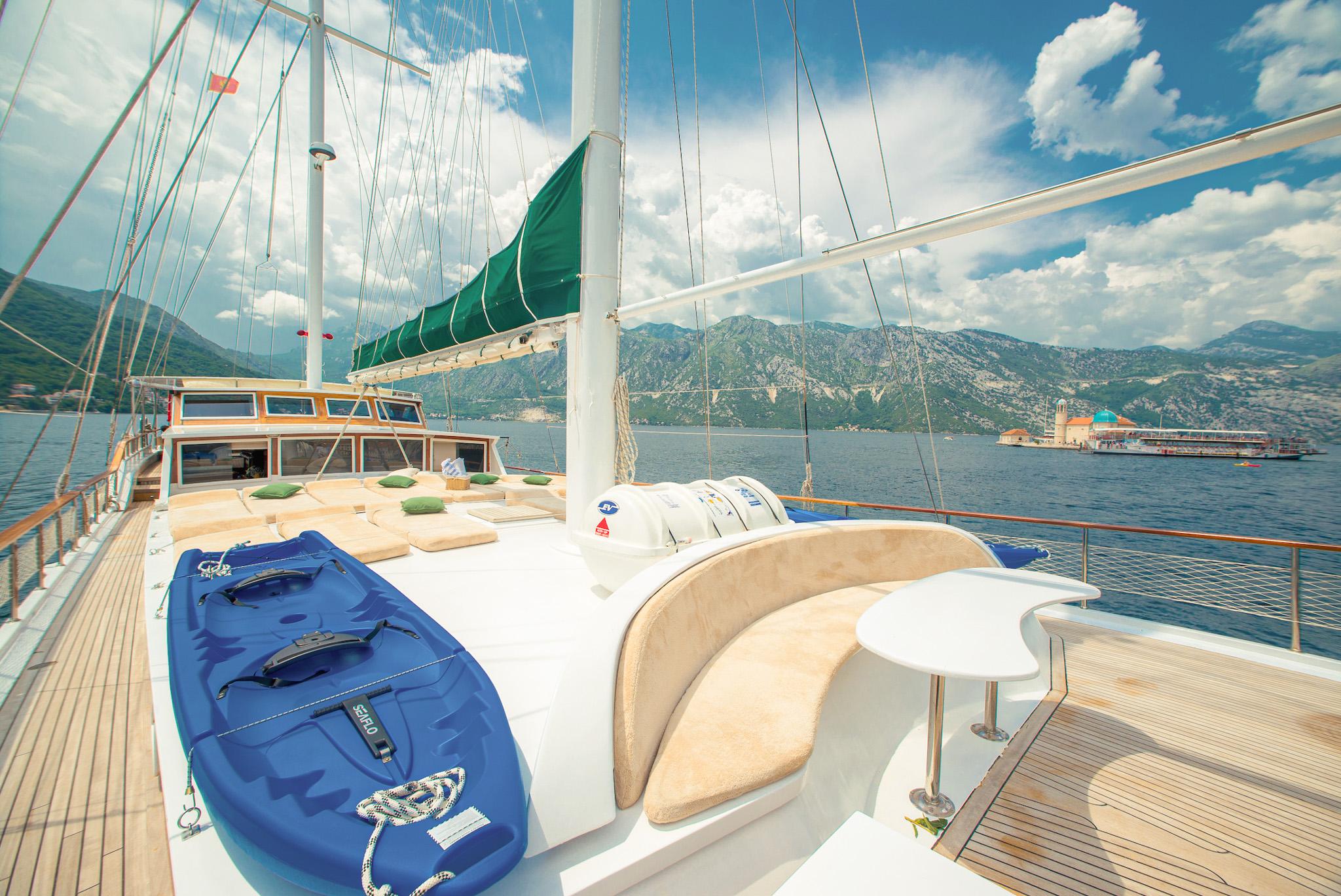 Blue kayak water toy and cushioned bow seating on gulet foredeck with Bay of Kotor mountains backdrop