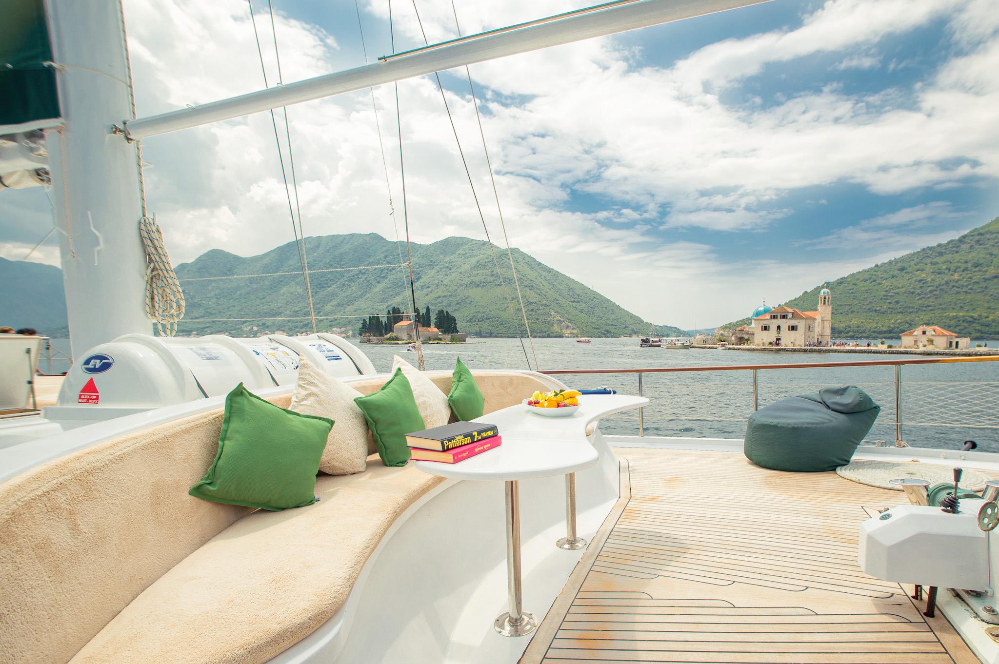 gulet aft deck curved cream sofa with green cushions and small pedestal table overlooking Bay of Kotor