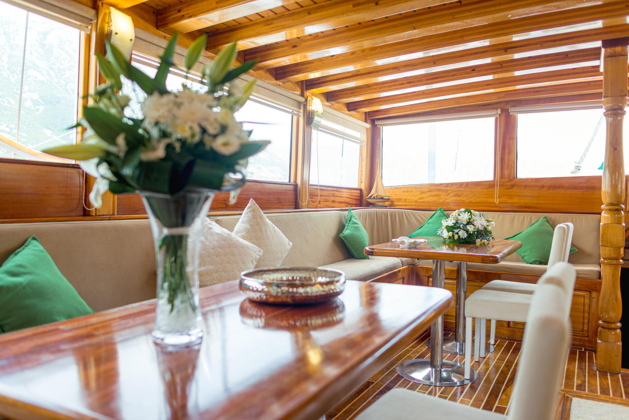 Gulet indoor saloon with varnished wood ceiling, cream and green cushioned bench seating, and polished dining tables