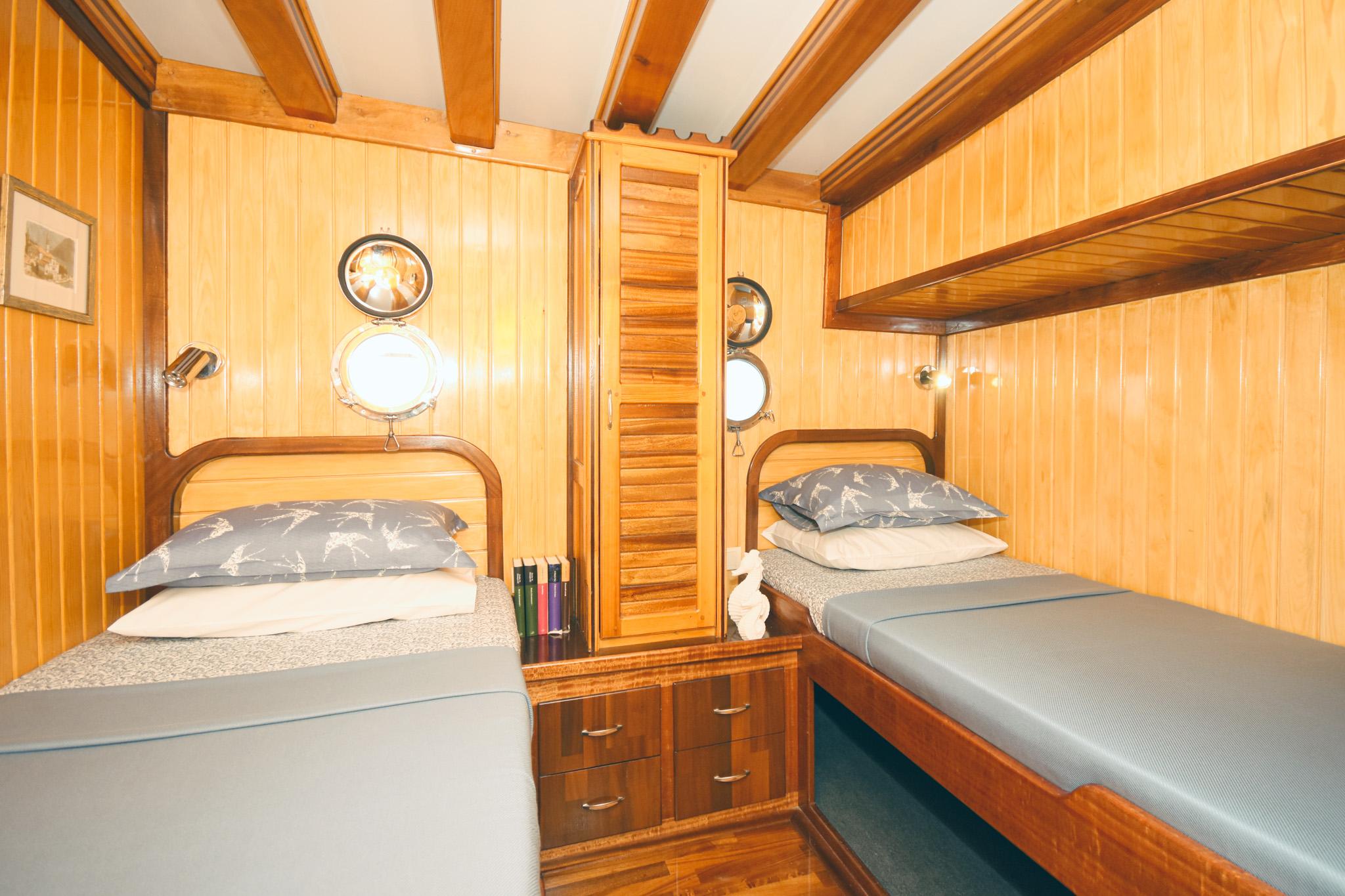 Gulet twin cabin with two single beds, louvred wardrobe, and brass portholes