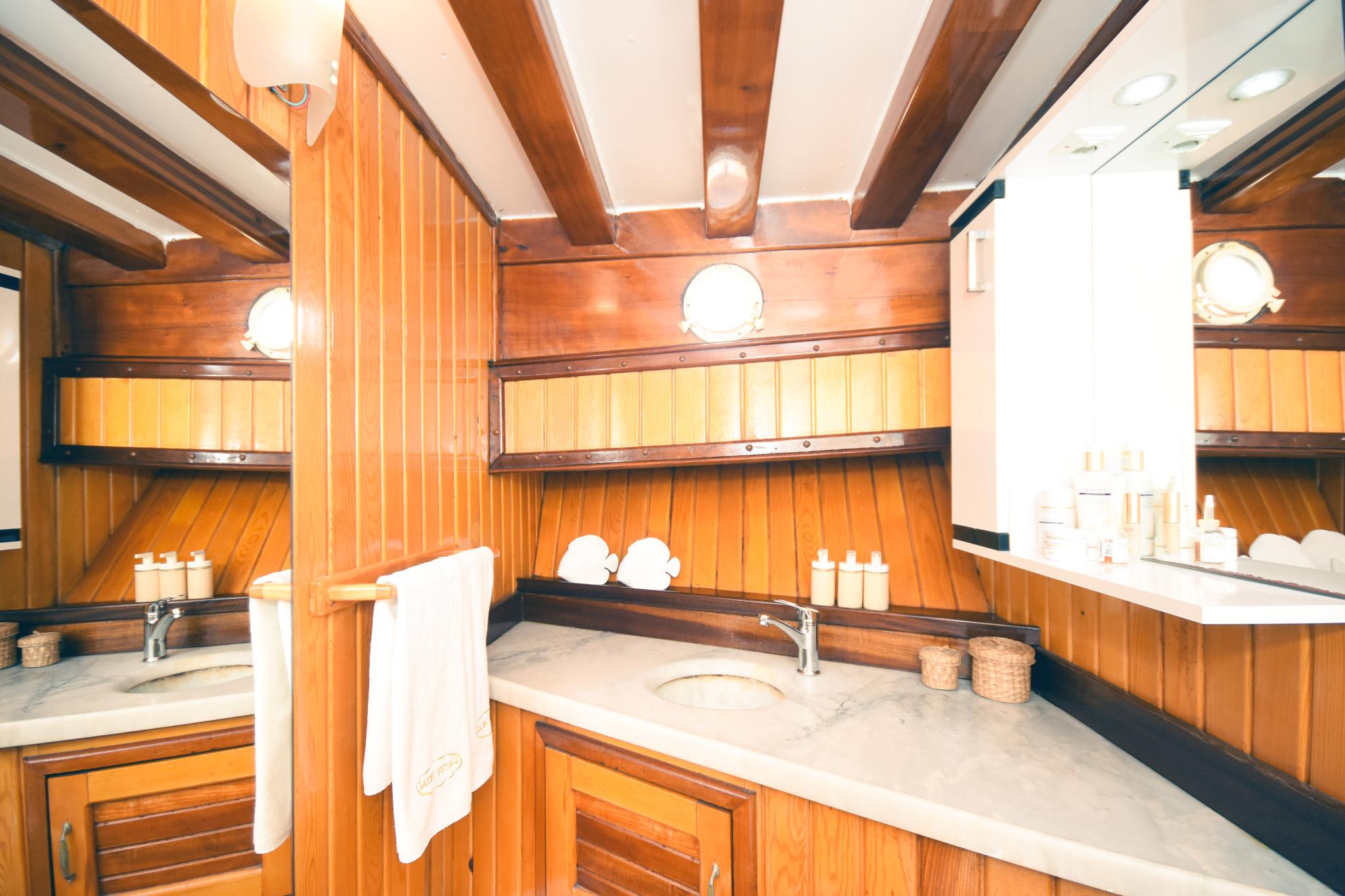 Gulet cabin bathroom with marble vanity twin sinks teak wood panelling and brass portholes