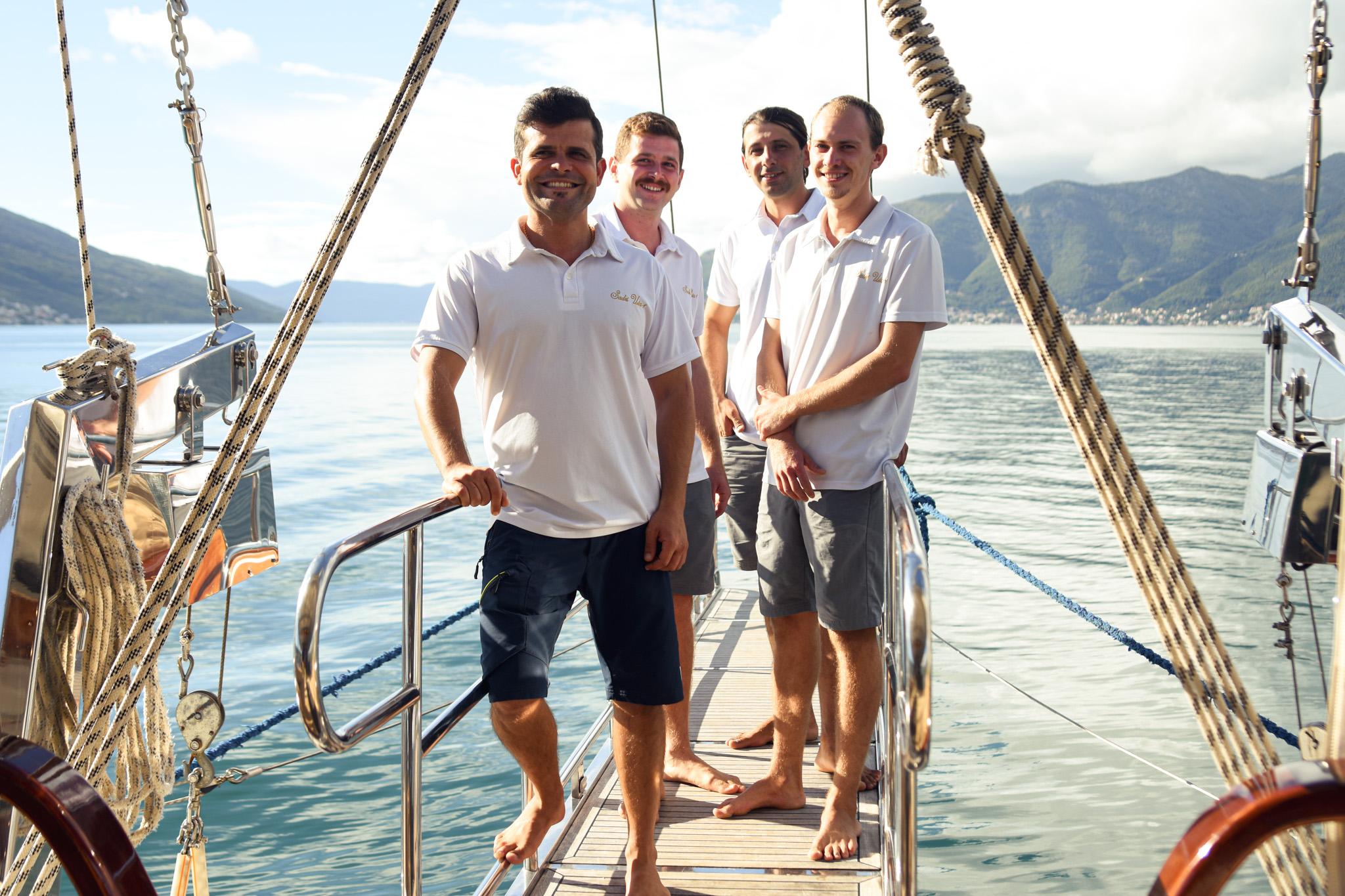 Four uniformed crew members smiling on gulet stern boarding platform with mountain backdrop