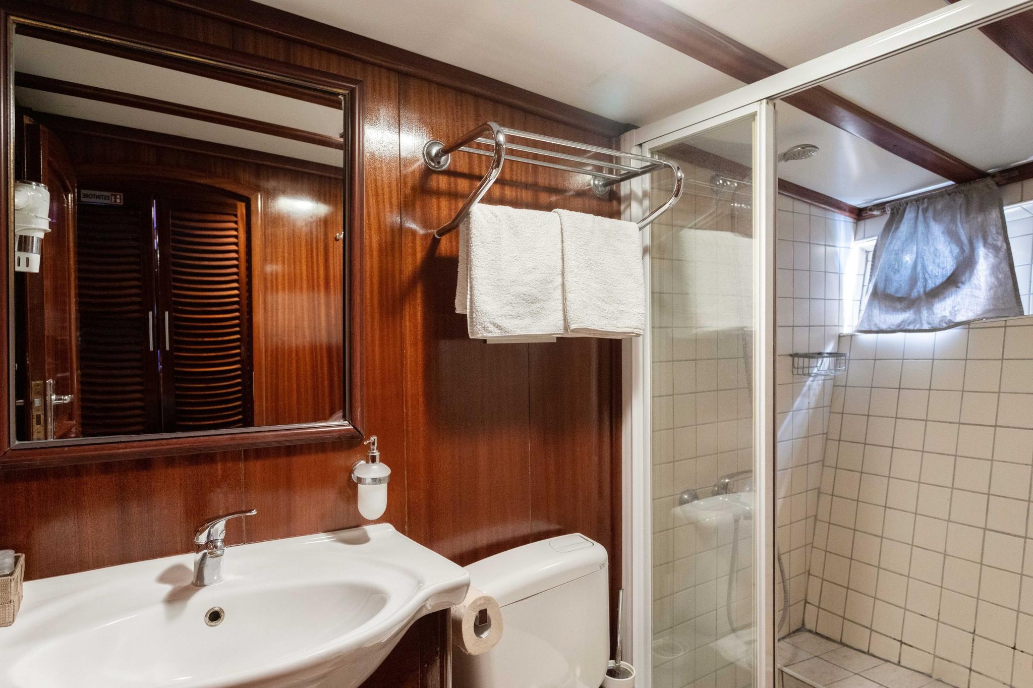 yacht bathroom featuring white basin, glass shower enclosure, and rich wood paneling