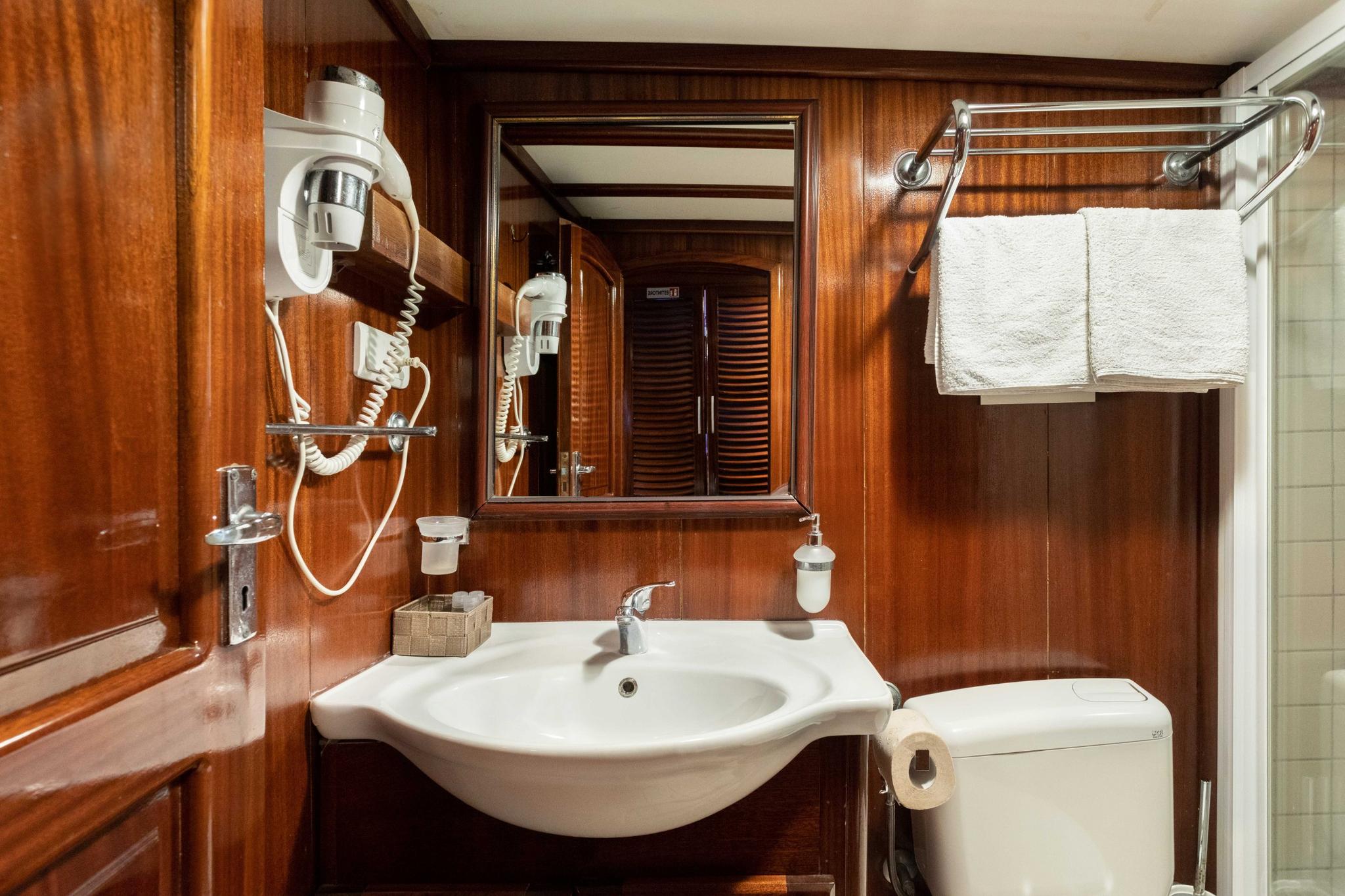 yacht en-suite bathroom with white basin, wood paneling, mirror and towel rail