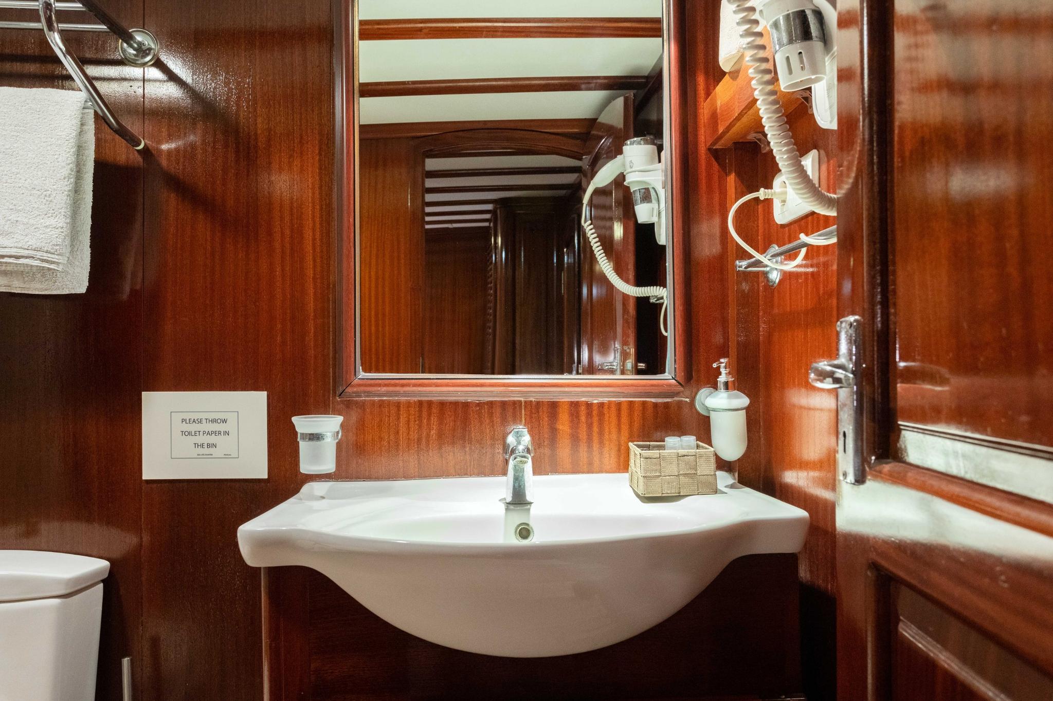 yacht bathroom featuring white ceramic basin, wooden wall paneling, mirror and hair dryer