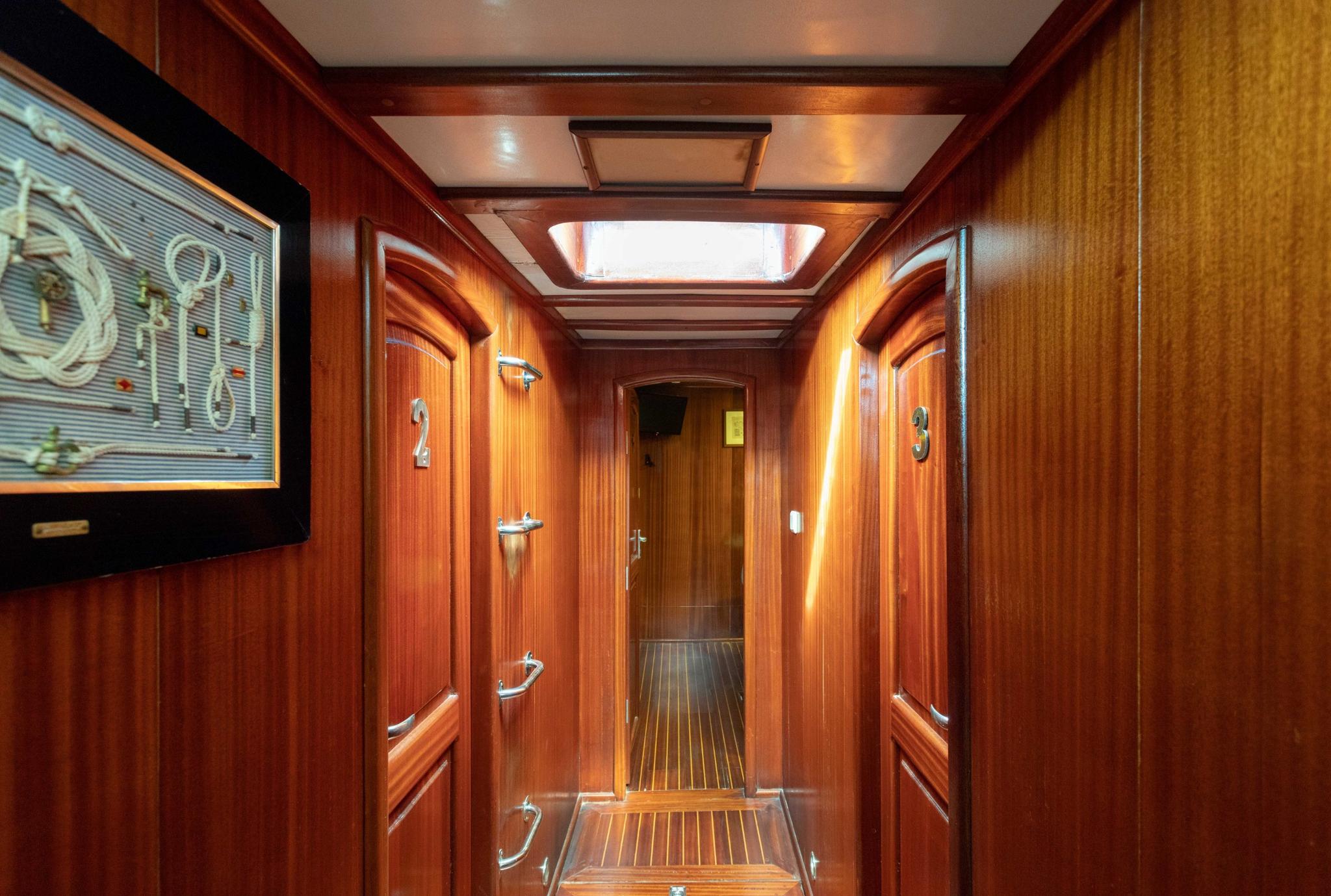 yacht interior corridor with rich wood paneling, cabin doors, and overhead skylights
