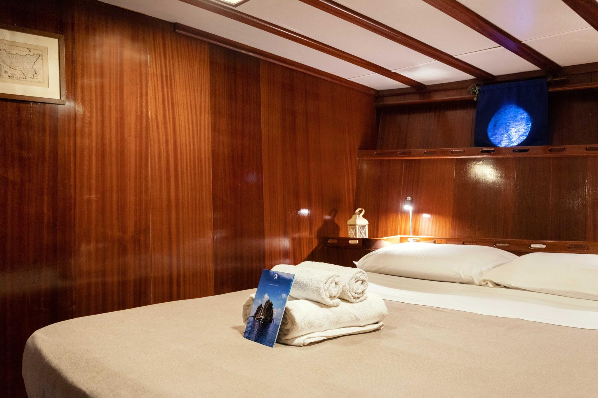 yacht cabin interior featuring double bed with white linens and built-in wooden headboard storage
