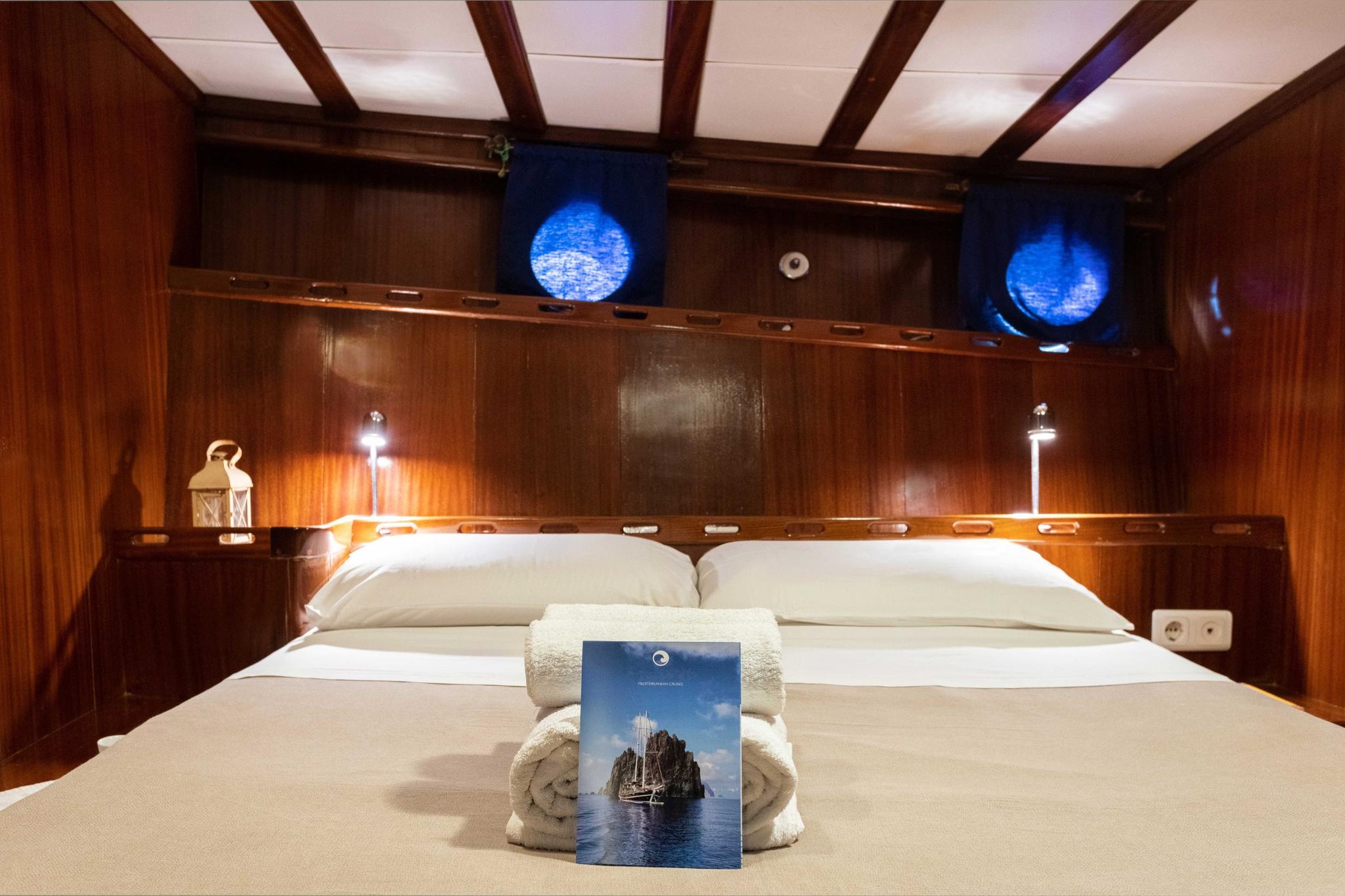 yacht cabin with double bed, wood paneling, and illuminated portholes