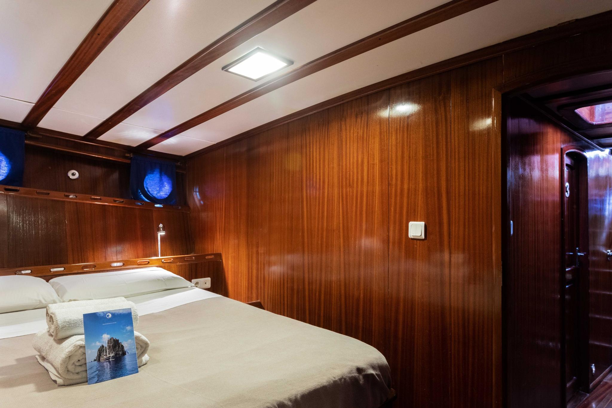 yacht guest cabin featuring double bed, polished wood walls, built-in headboard with reading lights