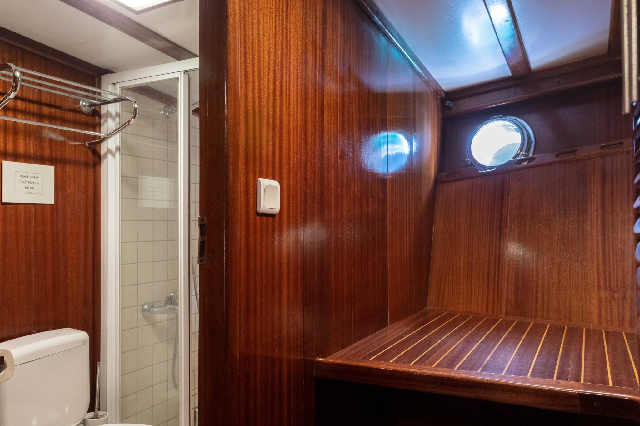 yacht sauna with wooden bench seating, porthole window, and adjacent shower compartment