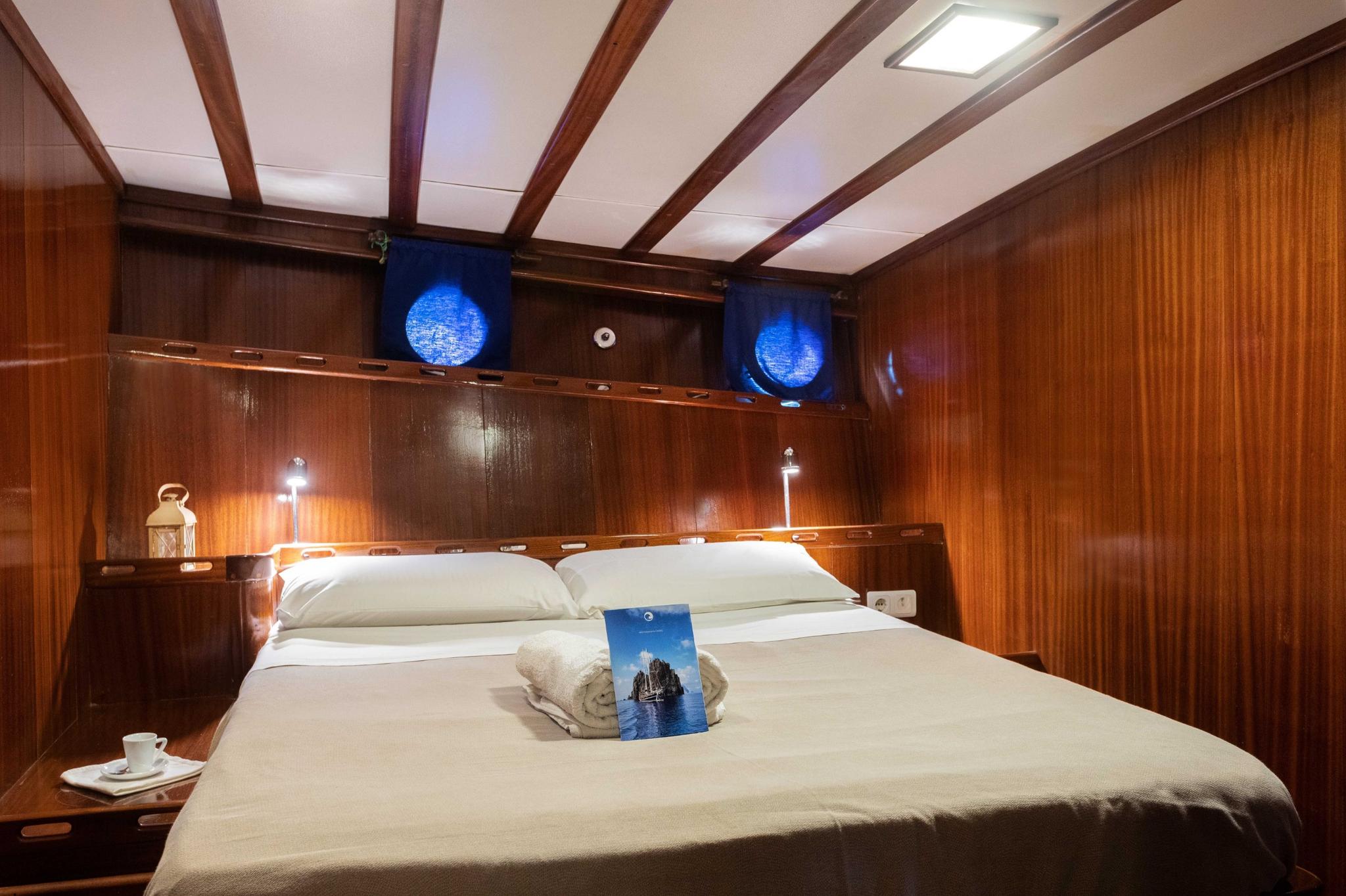 yacht cabin interior with double bed, wood paneling, portholes, and reading lights