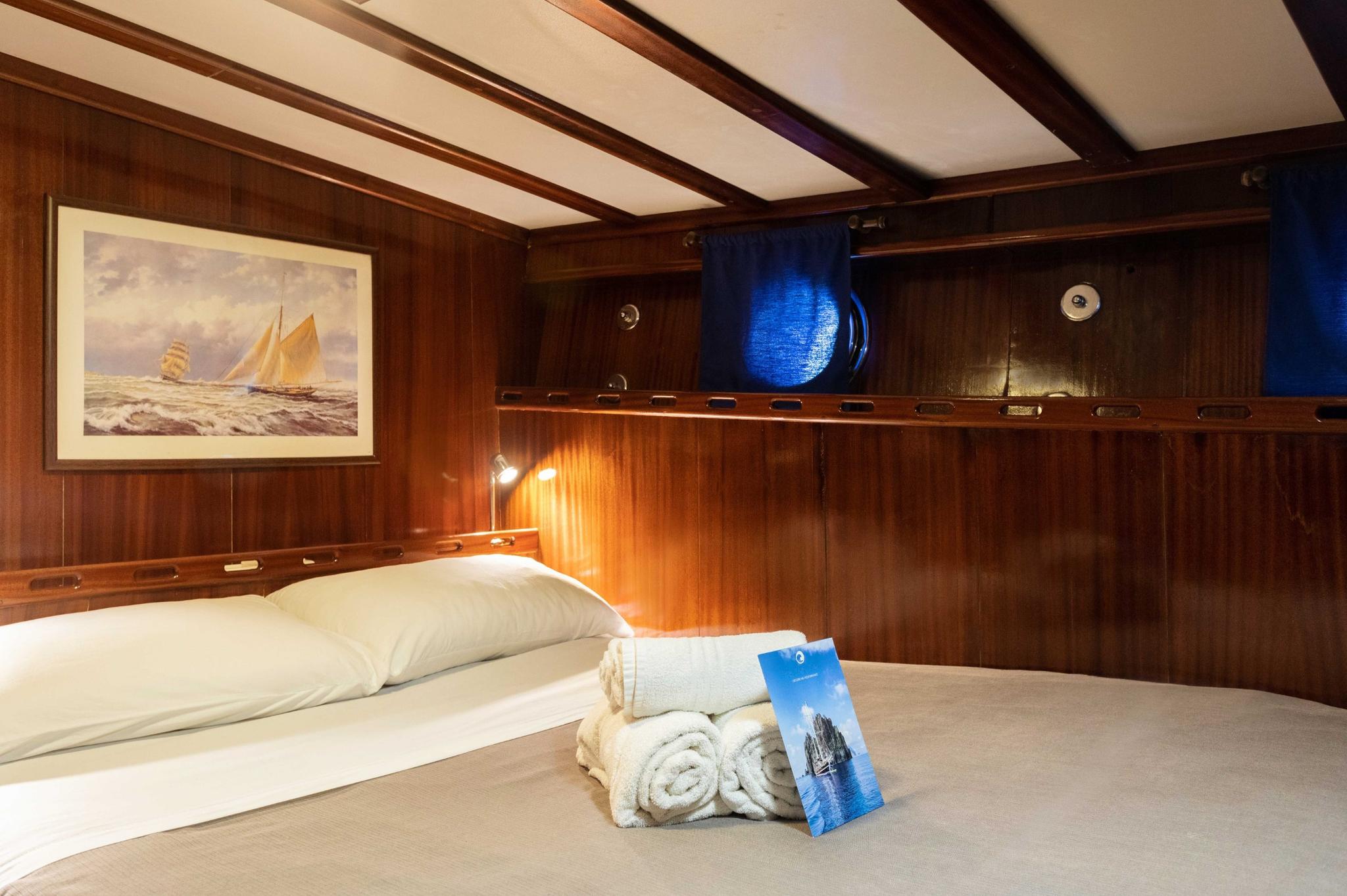 yacht cabin with double bed, wooden paneling, nautical artwork and built-in shelving