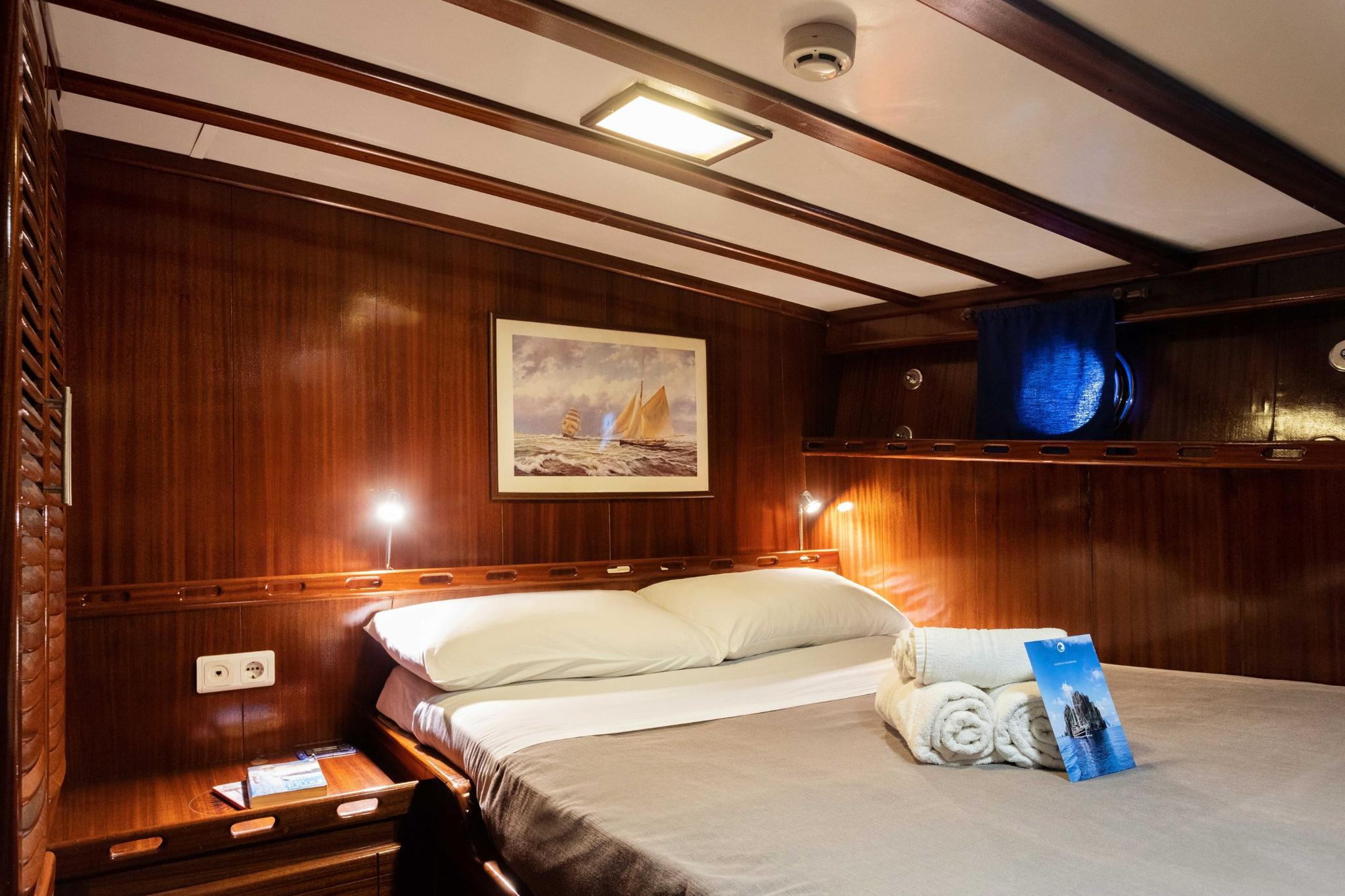yacht cabin interior with double bed, wooden paneling, nautical artwork and reading lights