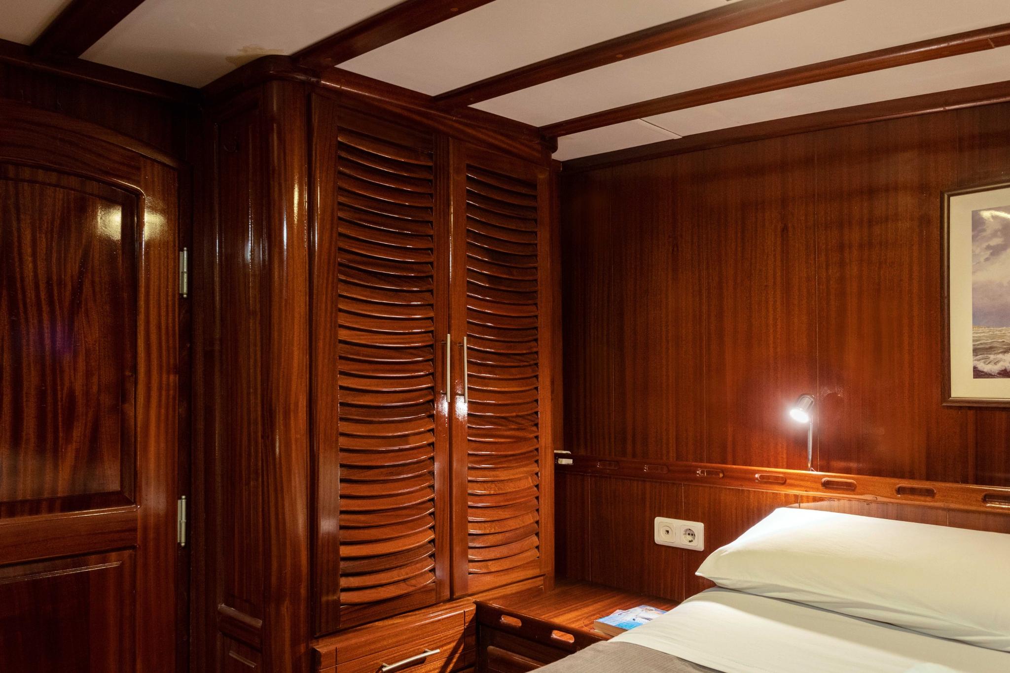 yacht cabin with rich wood paneling, louvered wardrobe doors, built-in bedside reading light and white bedding