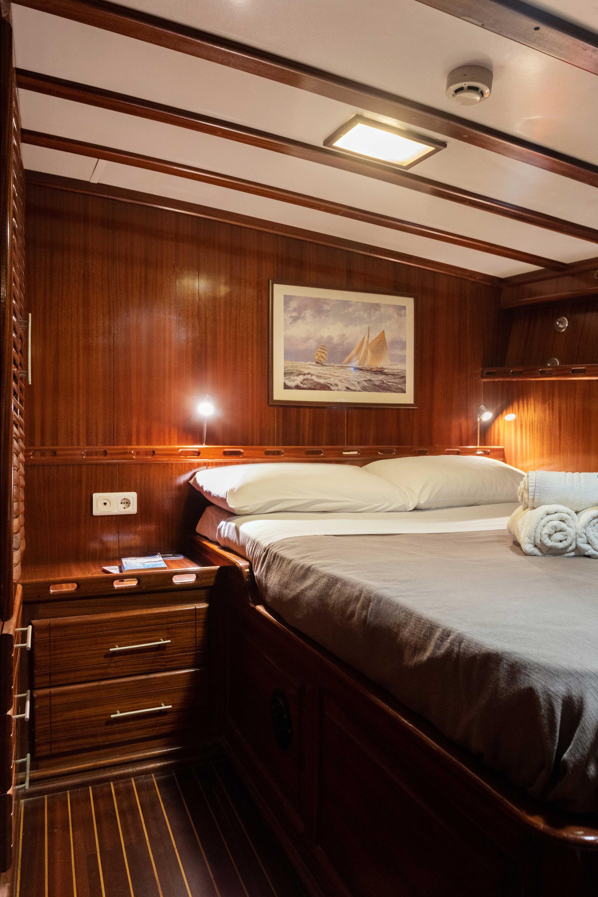 yacht cabin interior featuring double bed with white linens, rich wood paneling, nautical artwork, and bedside reading lights