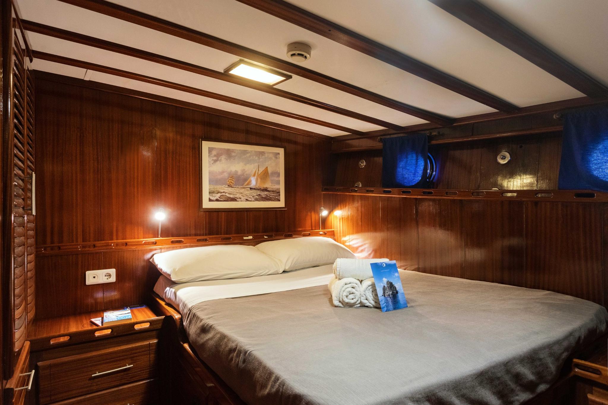 yacht guest cabin featuring double bed with white linens, rich wood paneling, nautical artwork, and built-in storage