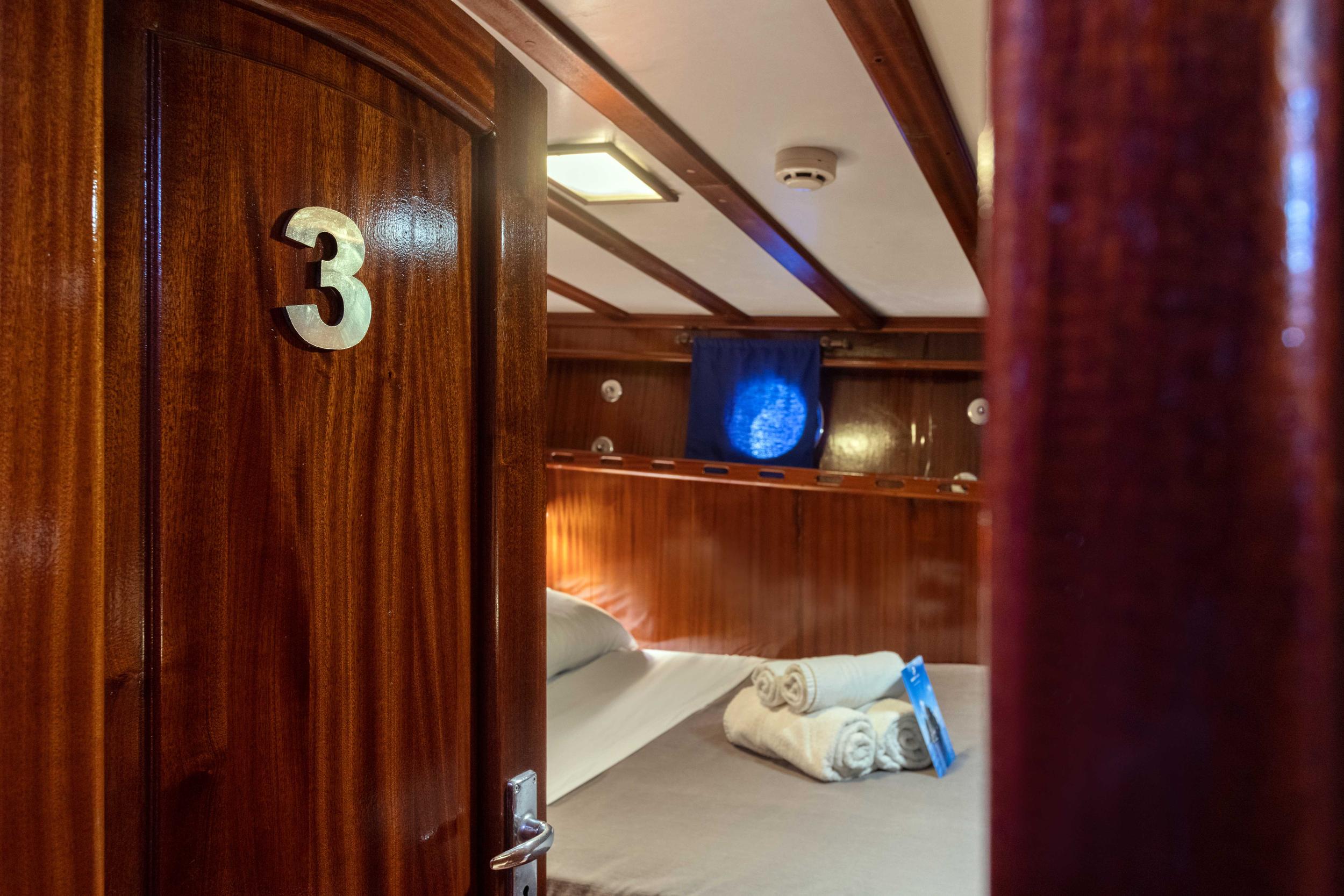 guest cabin 3 interior with twin beds, rich wood paneling and porthole window