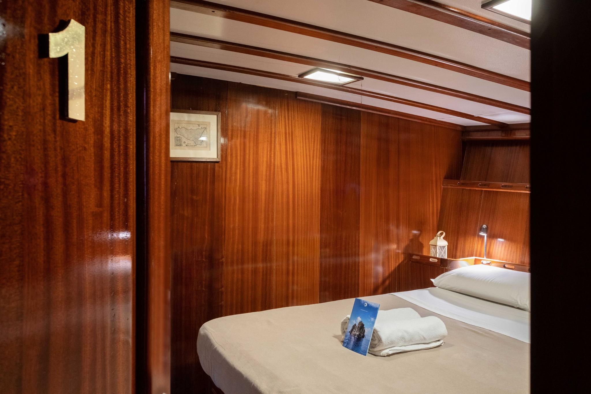 yacht guest cabin with double bed, rich wood paneling, nautical chart artwork and reading lights