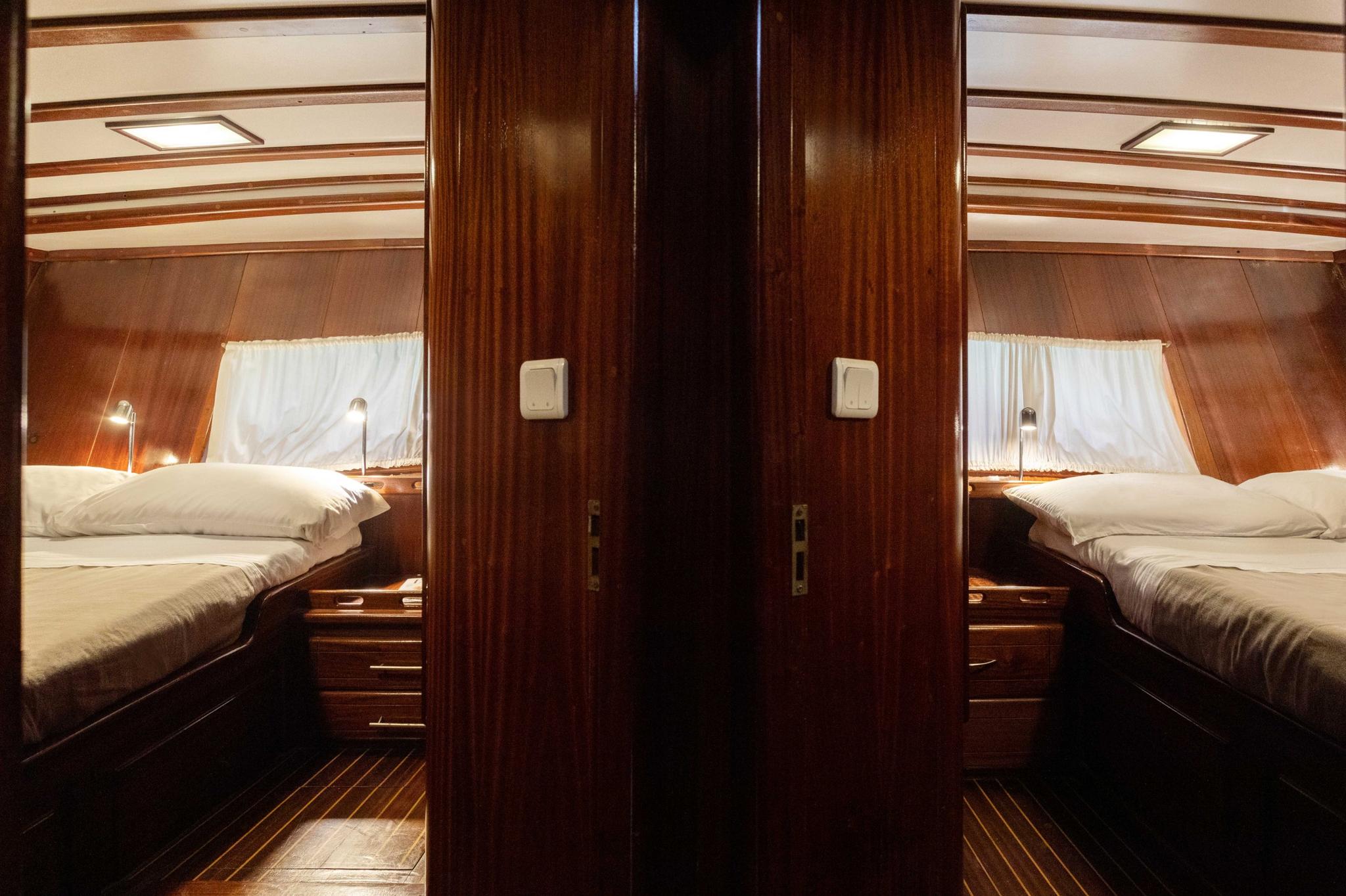 twin guest cabins with single beds, wooden paneling, portholes and reading lights