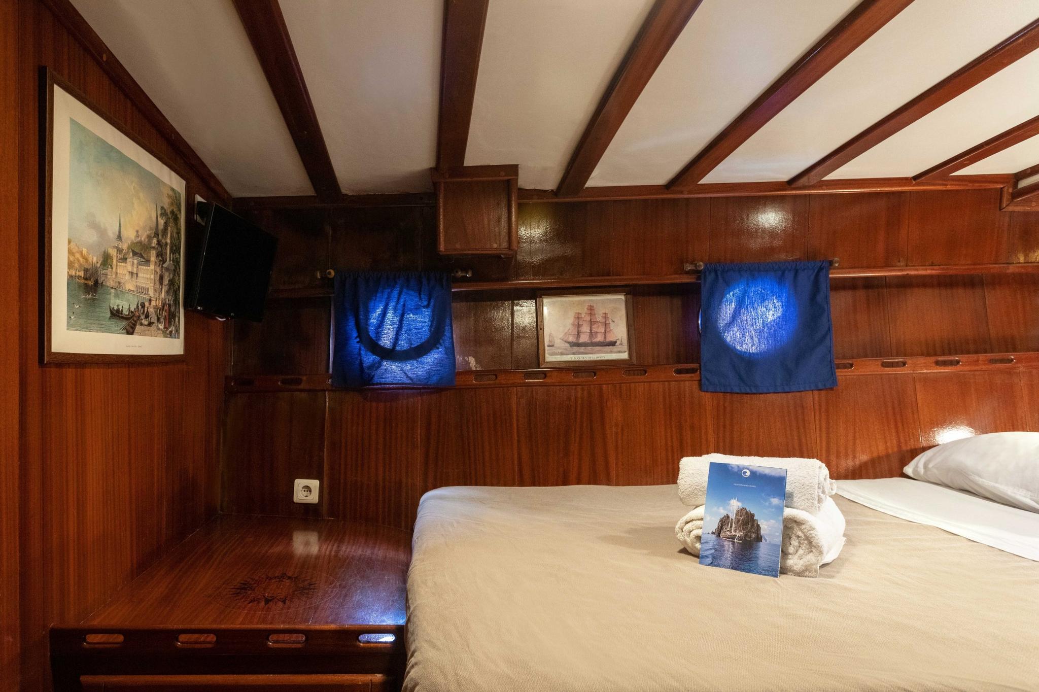 yacht guest cabin featuring twin beds, exposed wooden beams, maritime artwork and blue towels