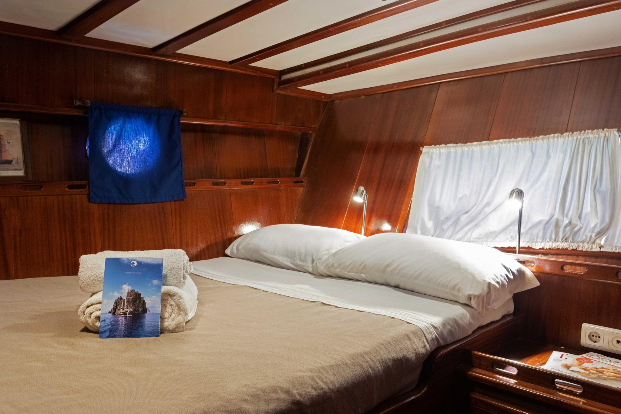 yacht guest cabin featuring double bed with white linens and rich wooden paneling