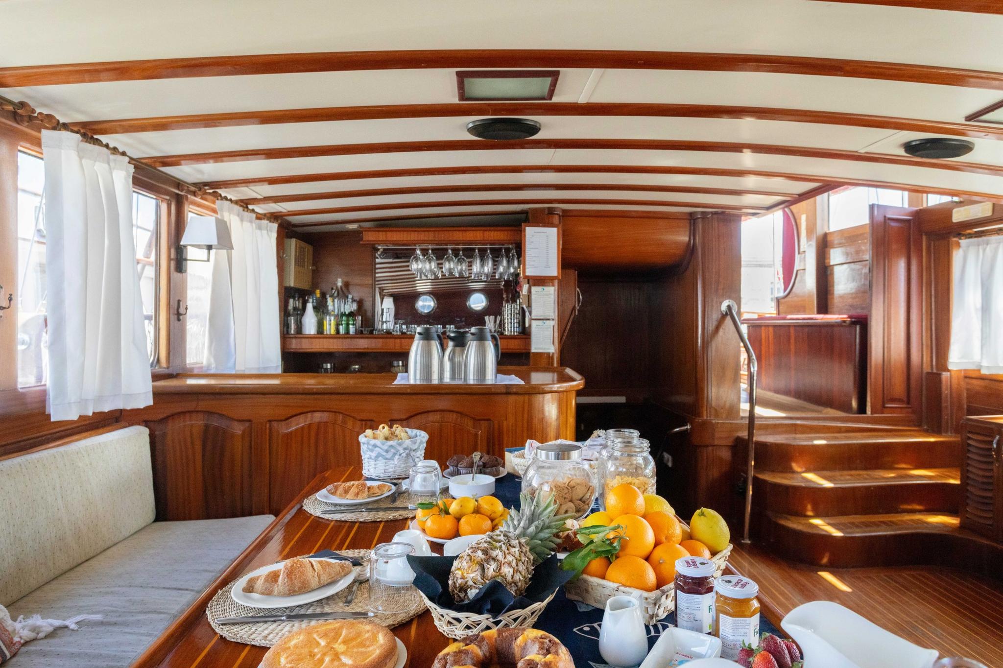 gulet interior dining table with breakfast spread featuring fresh fruits pastries and beverages