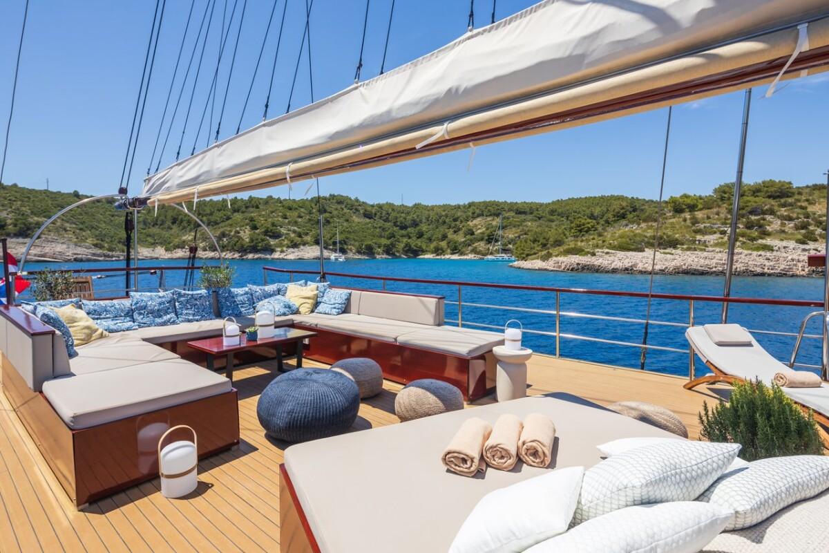 Luxury yacht aft deck with teak flooring, built-in seating, and Mediterranean coastline view