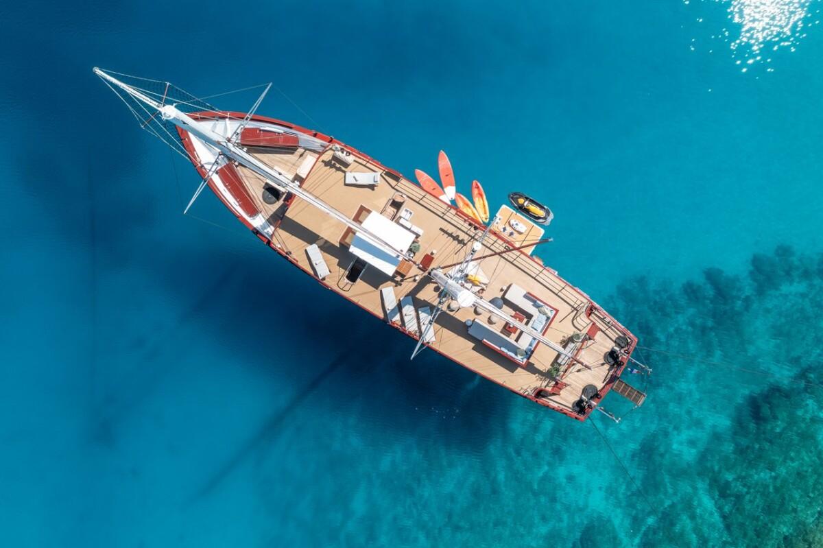 Aerial view of white sailing yacht with red trim anchored in crystal clear turquoise waters