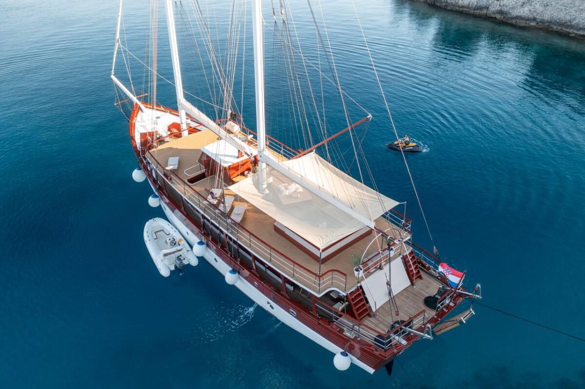 Aerial view of wooden gulet yacht with two masts anchored in clear blue water
