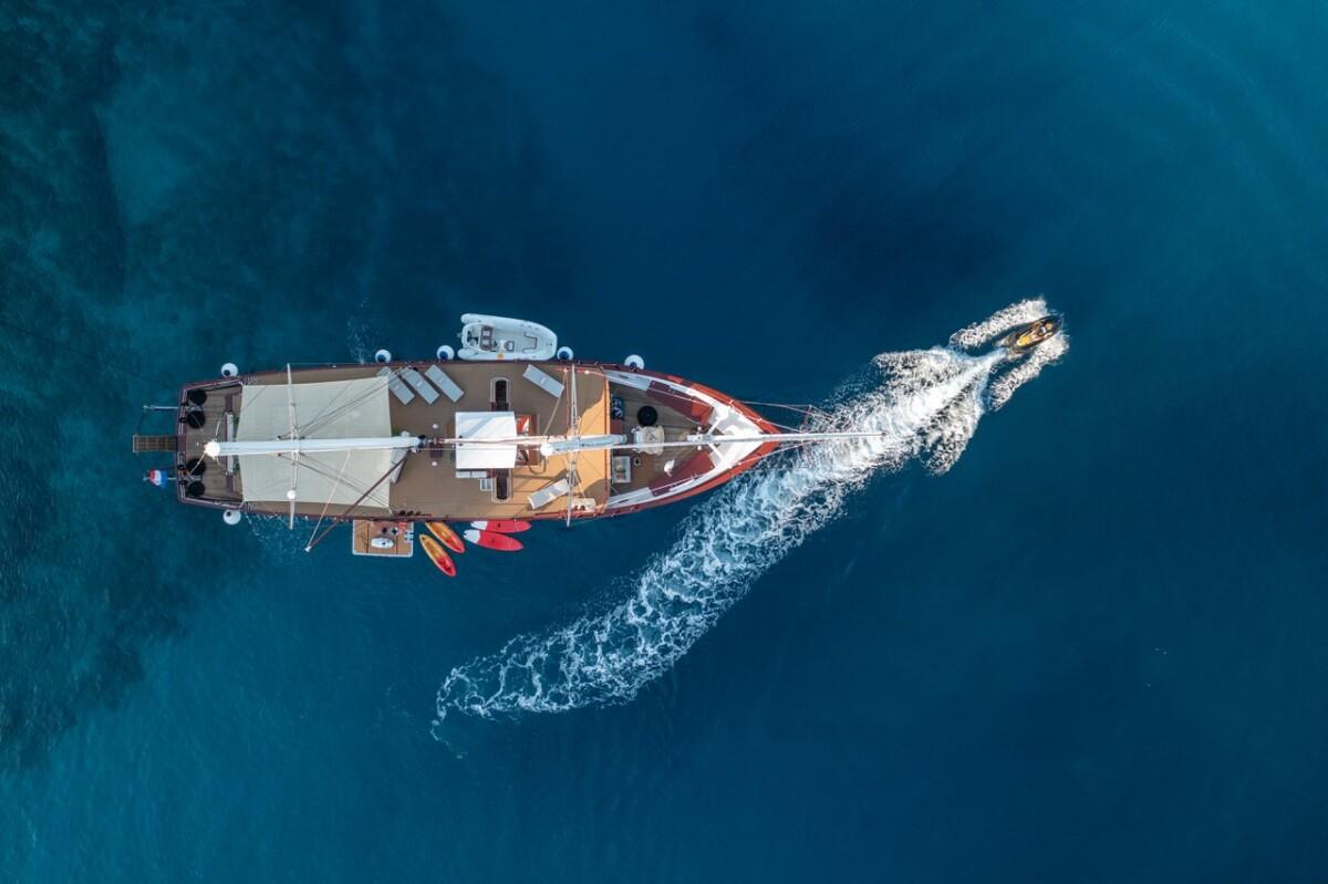 Aerial view of traditional gulet yacht under sail creating white wake in blue water