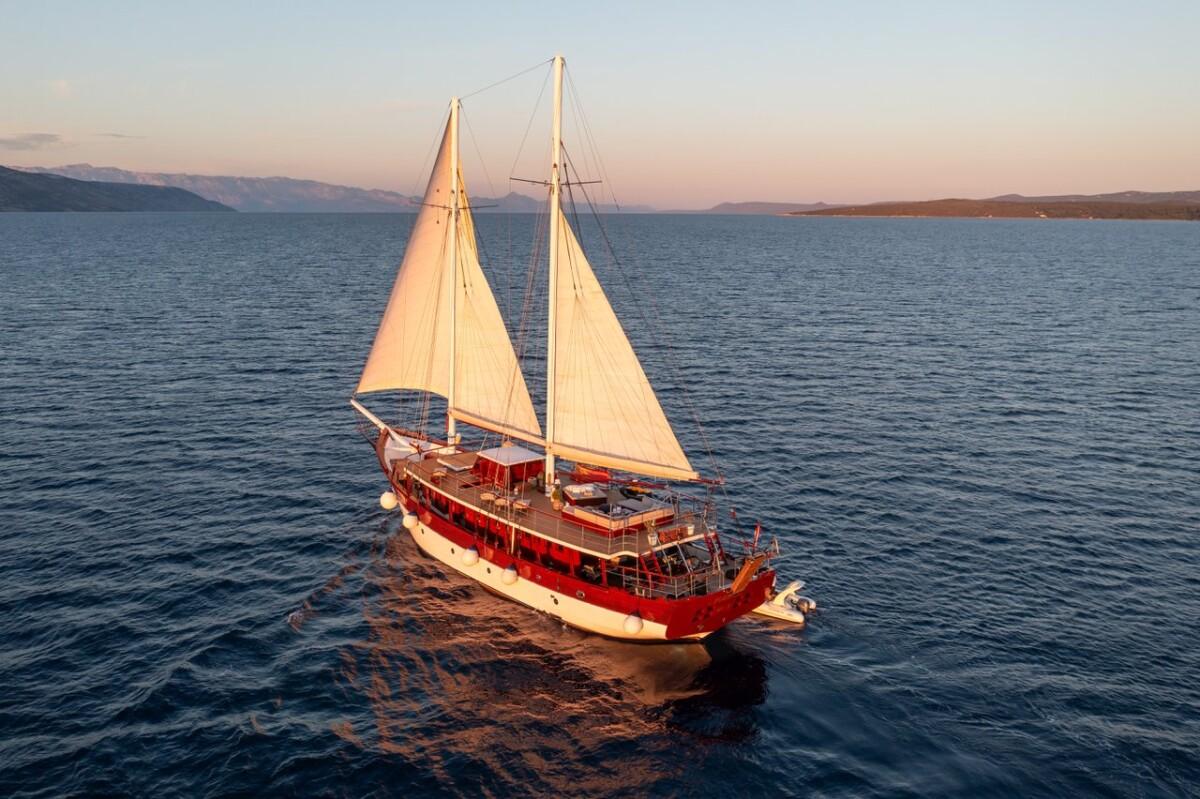 Traditional wooden gulet yacht sailing at sunset with two cream colored sails deployed