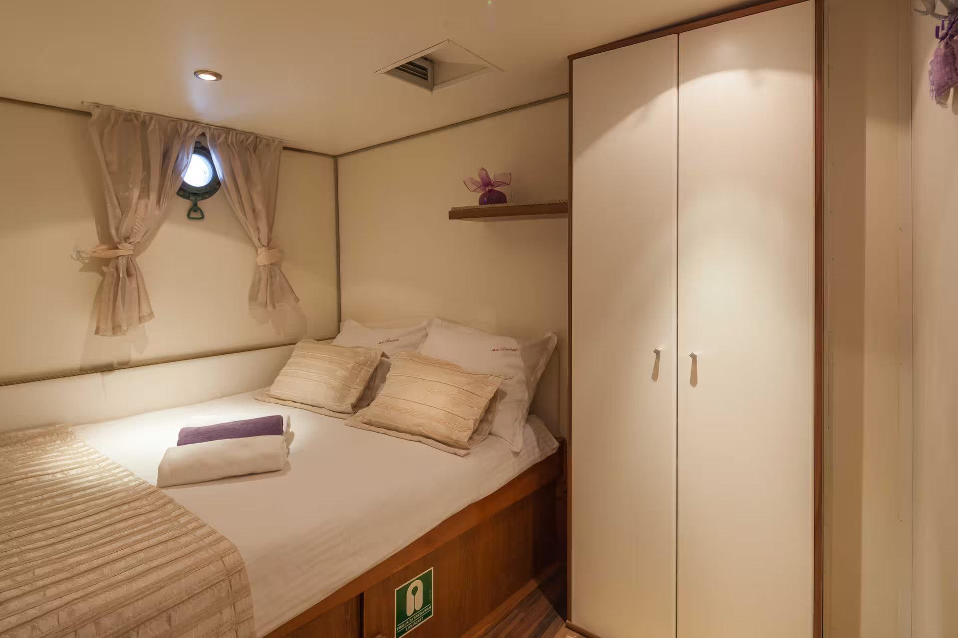 Gulet double cabin with white bedding, built-in wardrobe, and circular porthole window