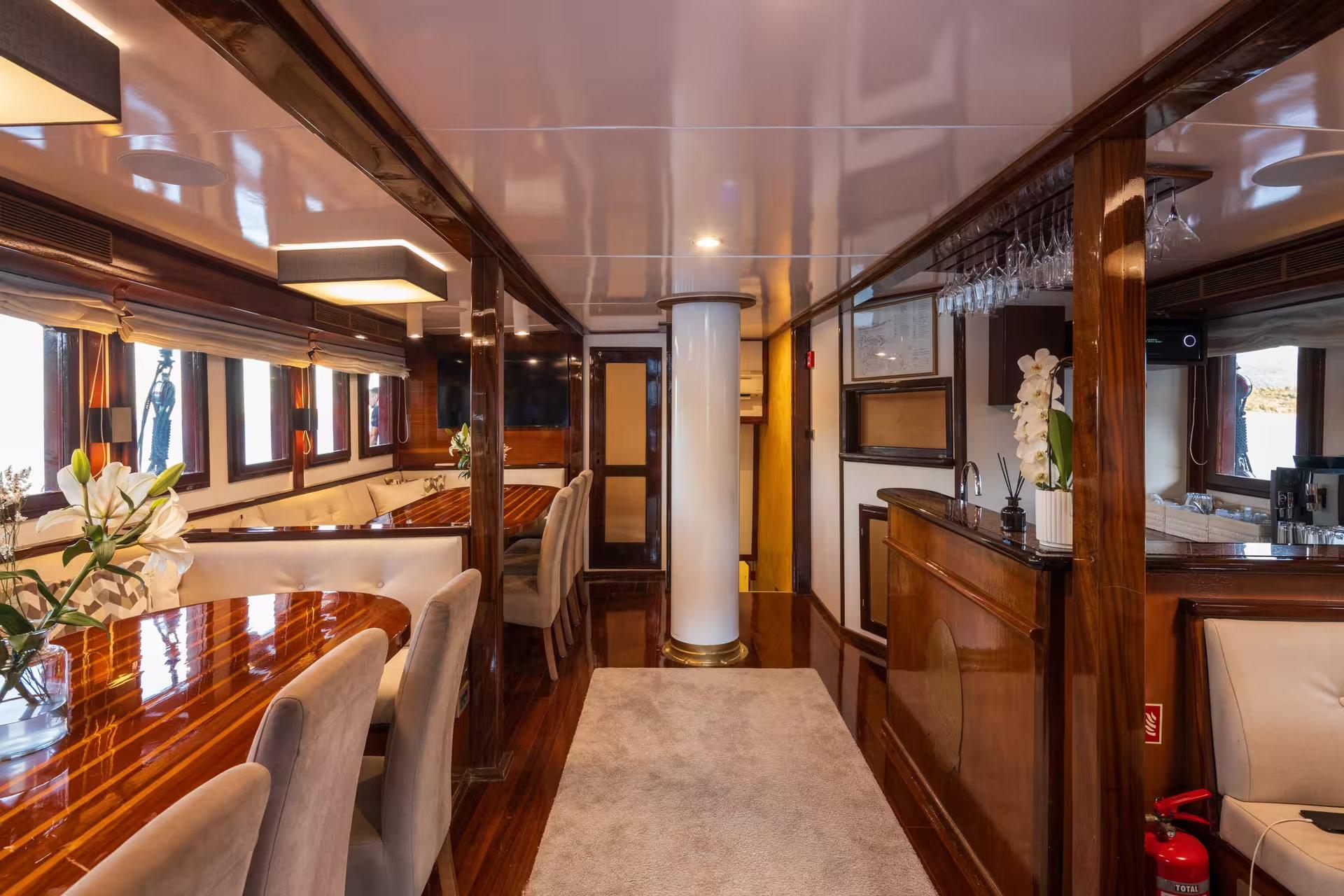 Luxury gulet saloon with polished wood dining table, upholstered chairs, wet bar with stemware rack, and white structural column