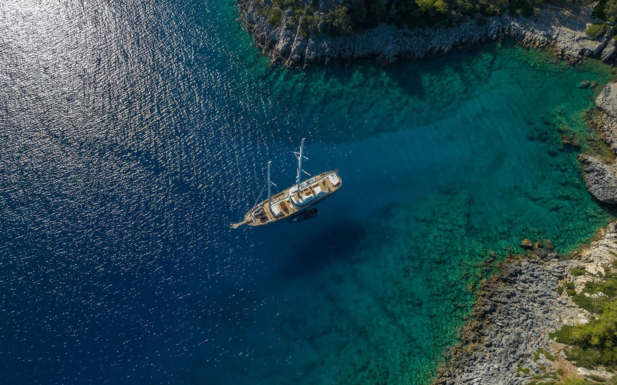 aerial view of wooden gulet yacht anchored in crystal clear turquoise bay surrounded by rocky coastline