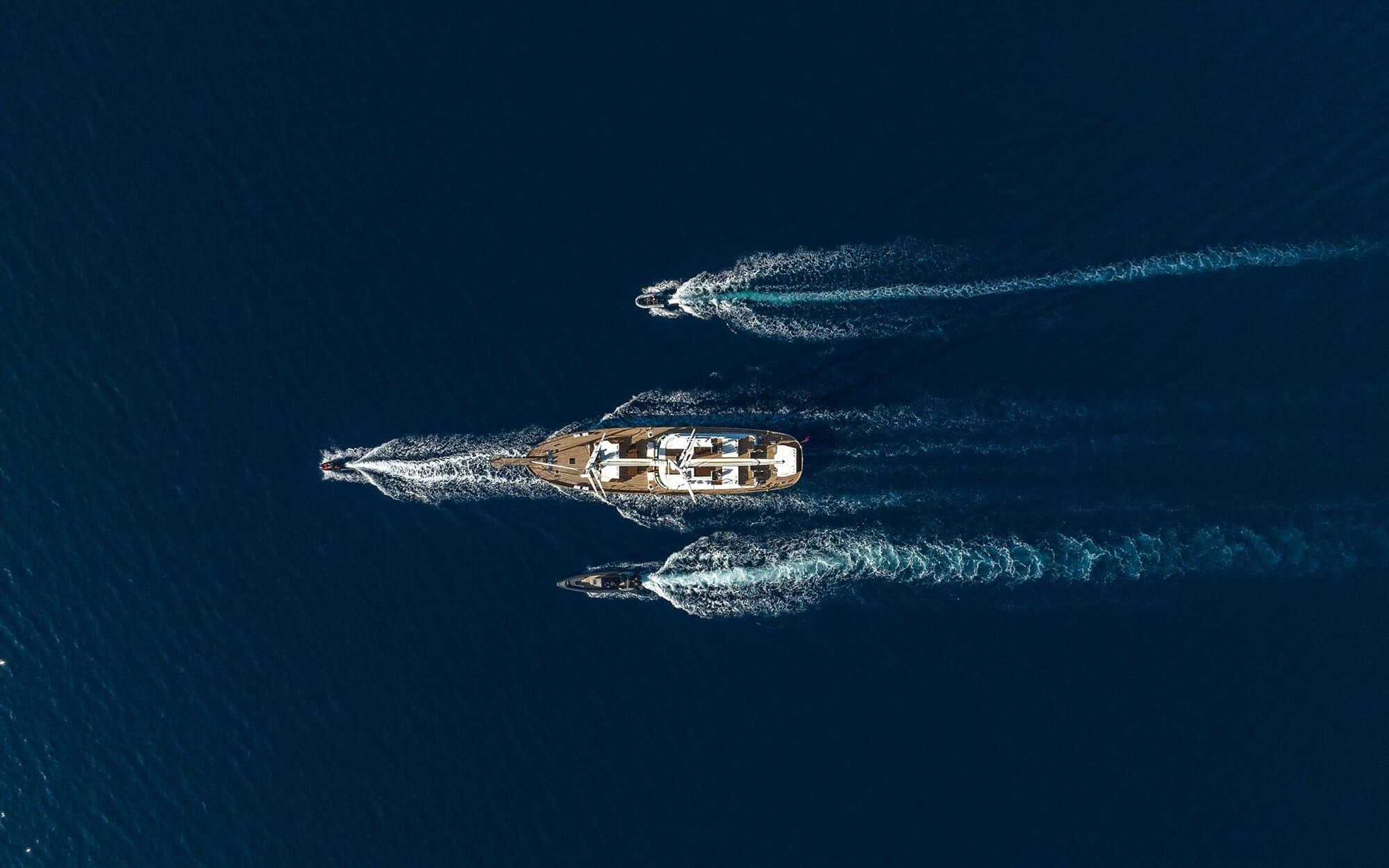 aerial drone shot of luxury yacht sailing with two escort boats creating wakes