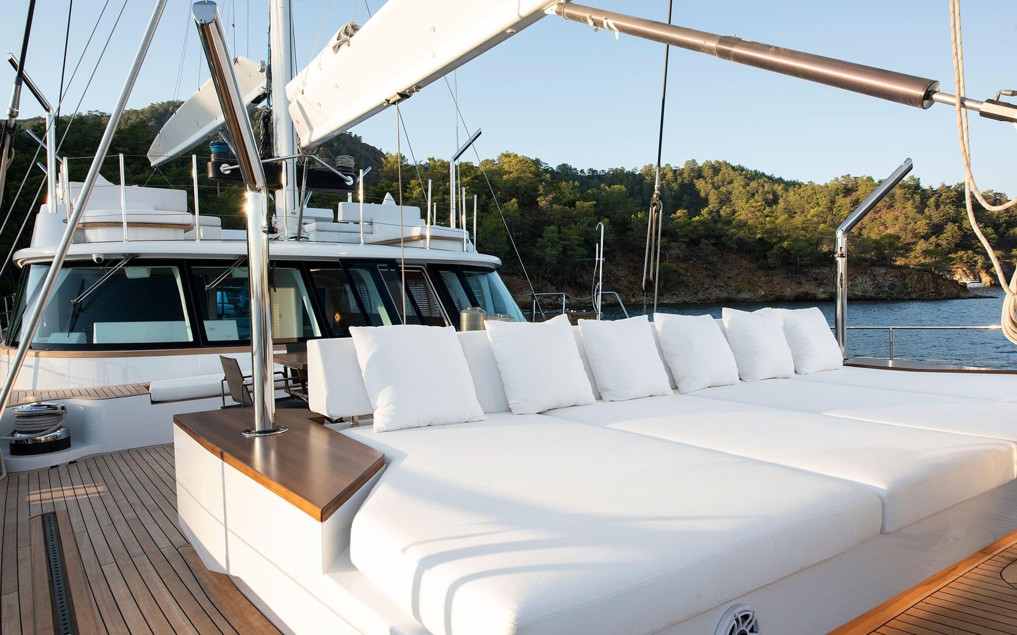 luxury yacht aft deck with white cushioned seating area and teak decking at anchor