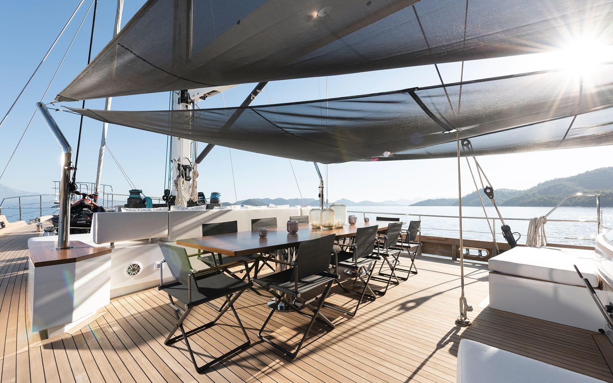 Yacht aft deck dining area with wooden table, folding chairs under fabric awning