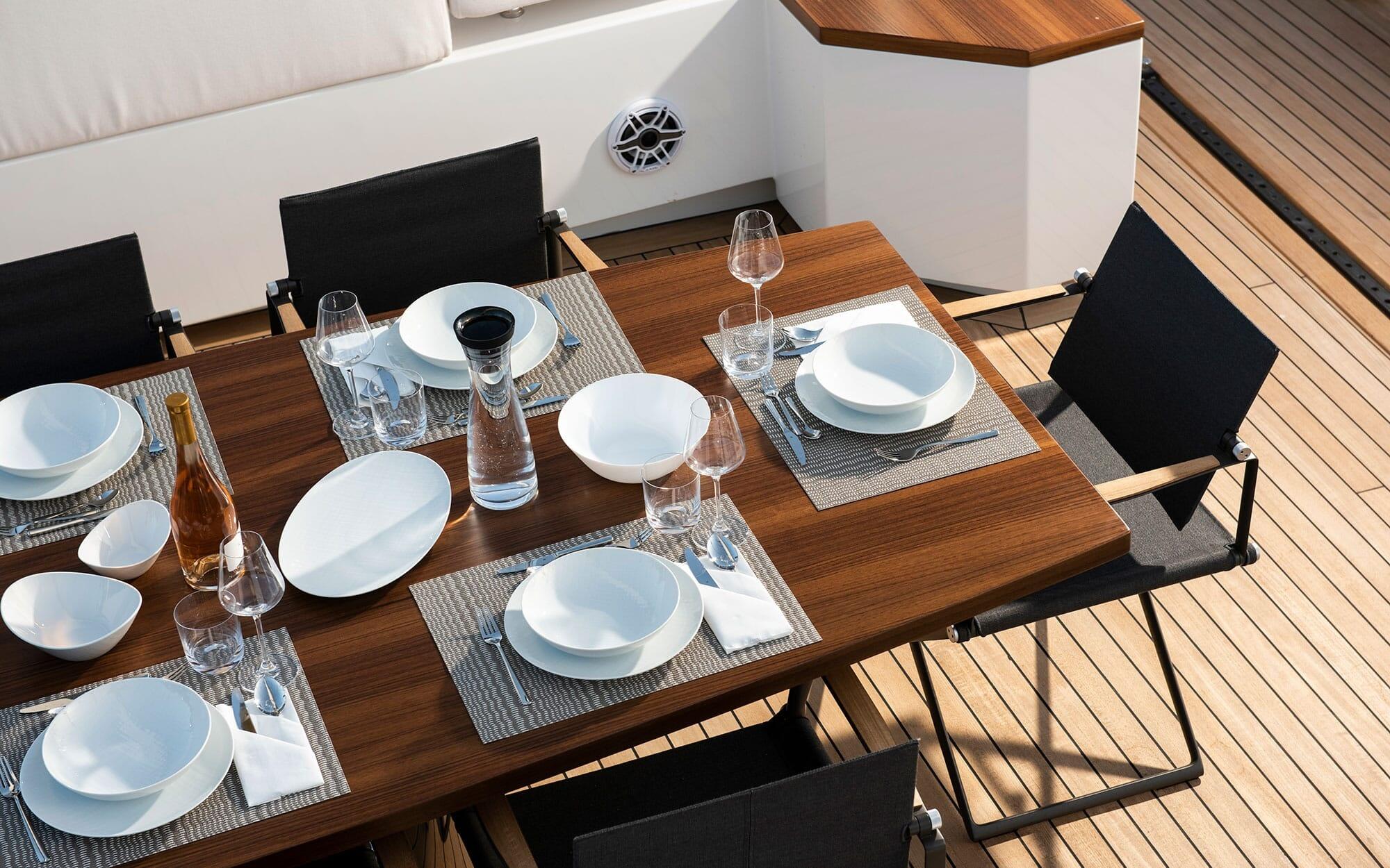 Teak dining table with white place settings and wine glasses on yacht aft deck