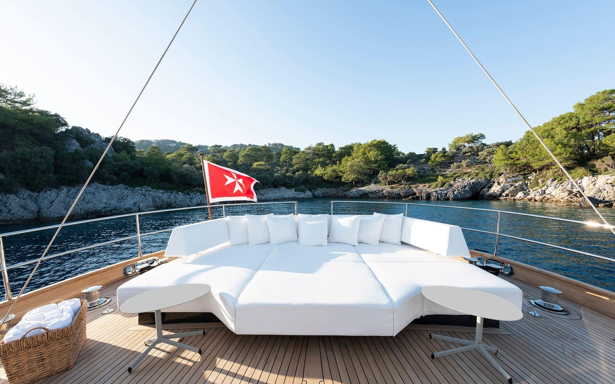 luxury yacht bow deck with curved white seating and red flag in secluded cove