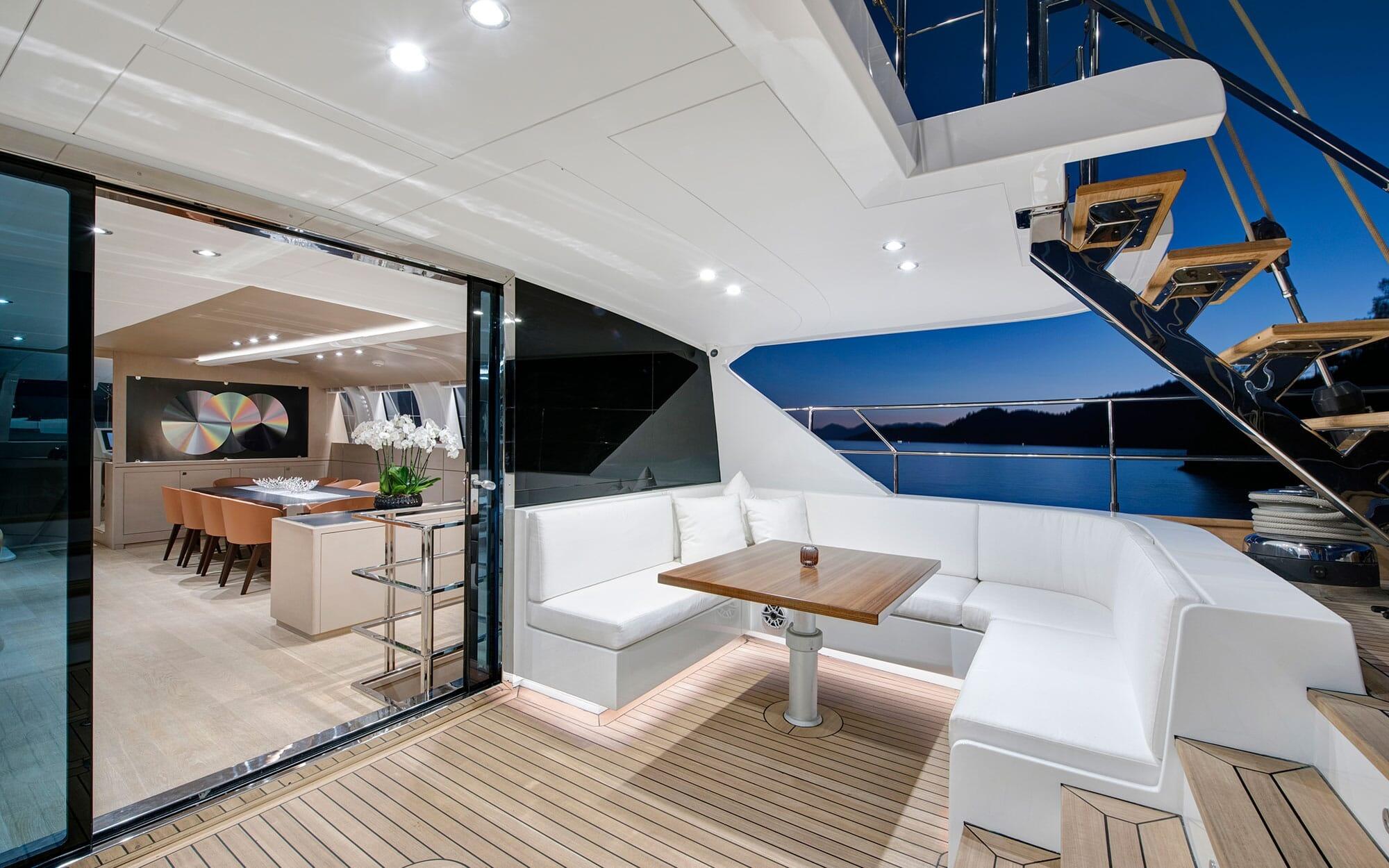 luxury yacht aft deck with white U-shaped seating and teak table overlooking interior dining salon