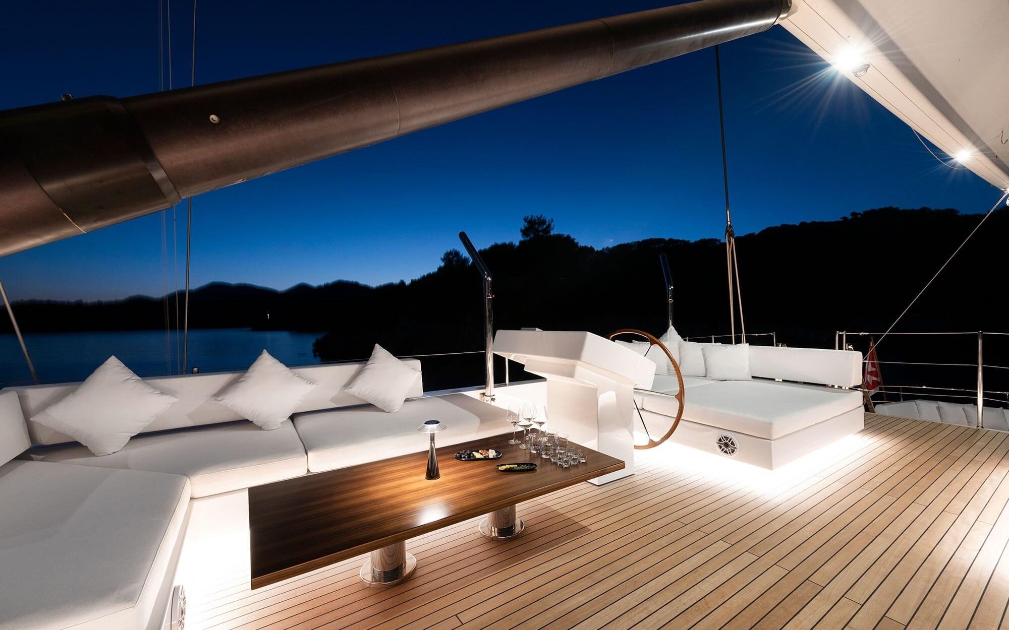 yacht aft deck with white cushioned seating area and teak decking under boom at twilight