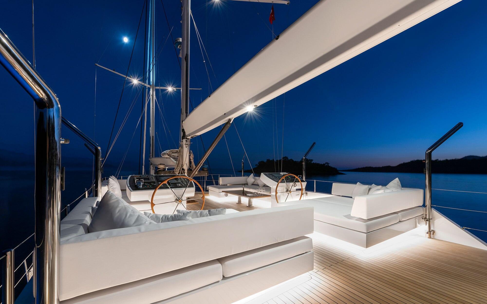 yacht cockpit with twin helm stations, white cushioned seating and wooden decking at twilight