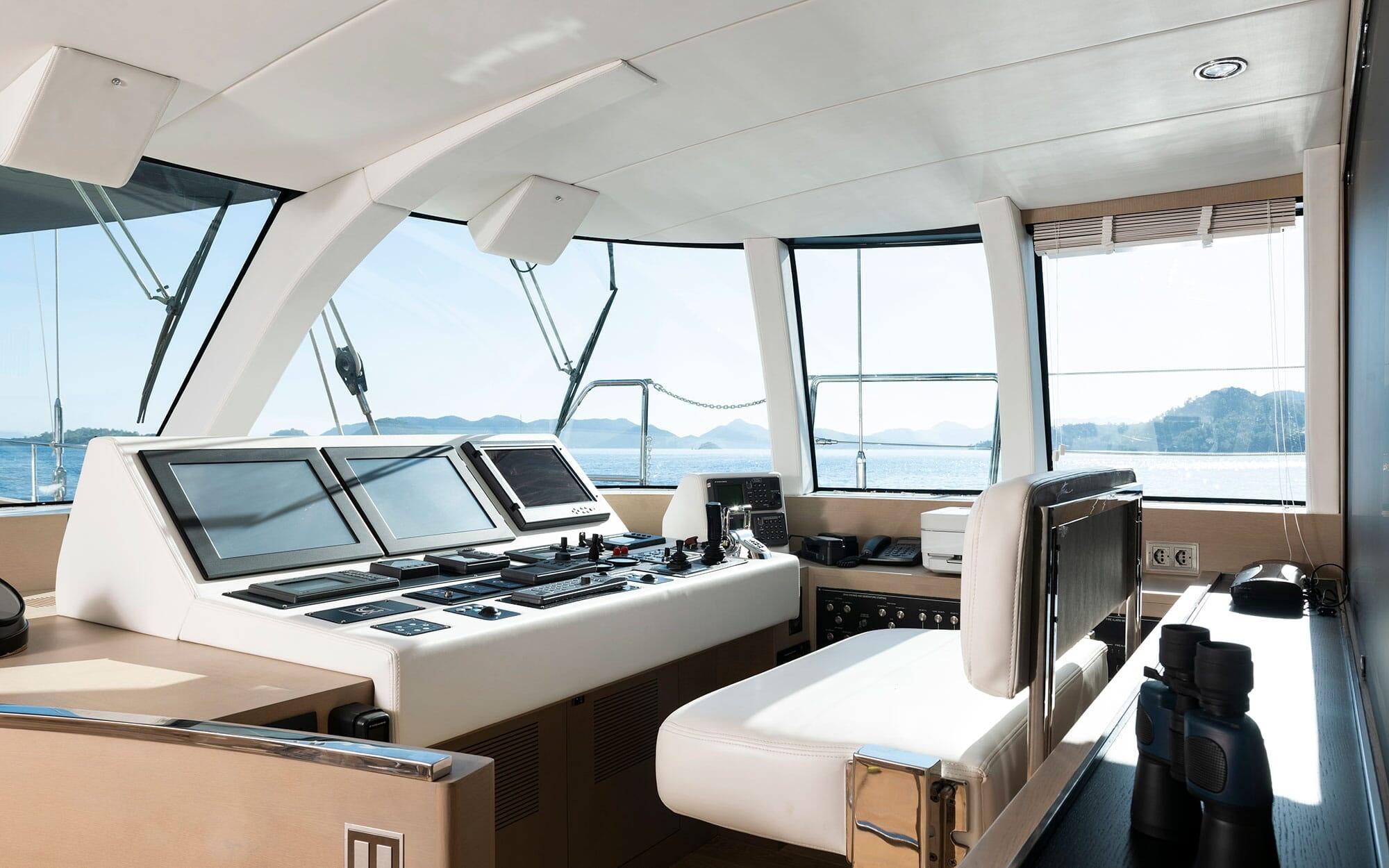 yacht helm station with multiple navigation screens, control panels and white captain's chair