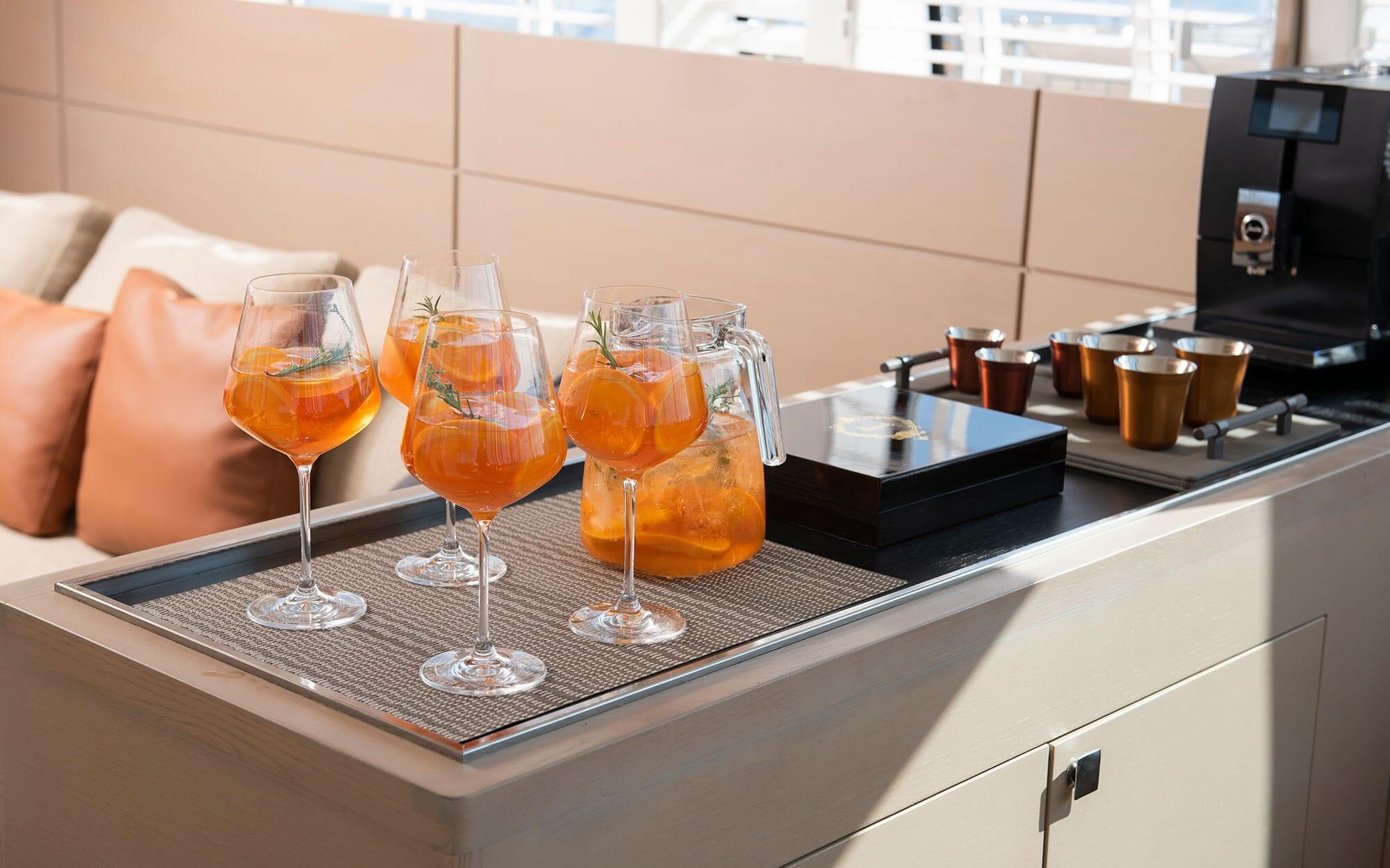 Orange cocktails with herb garnishes served on yacht galley counter with coffee station