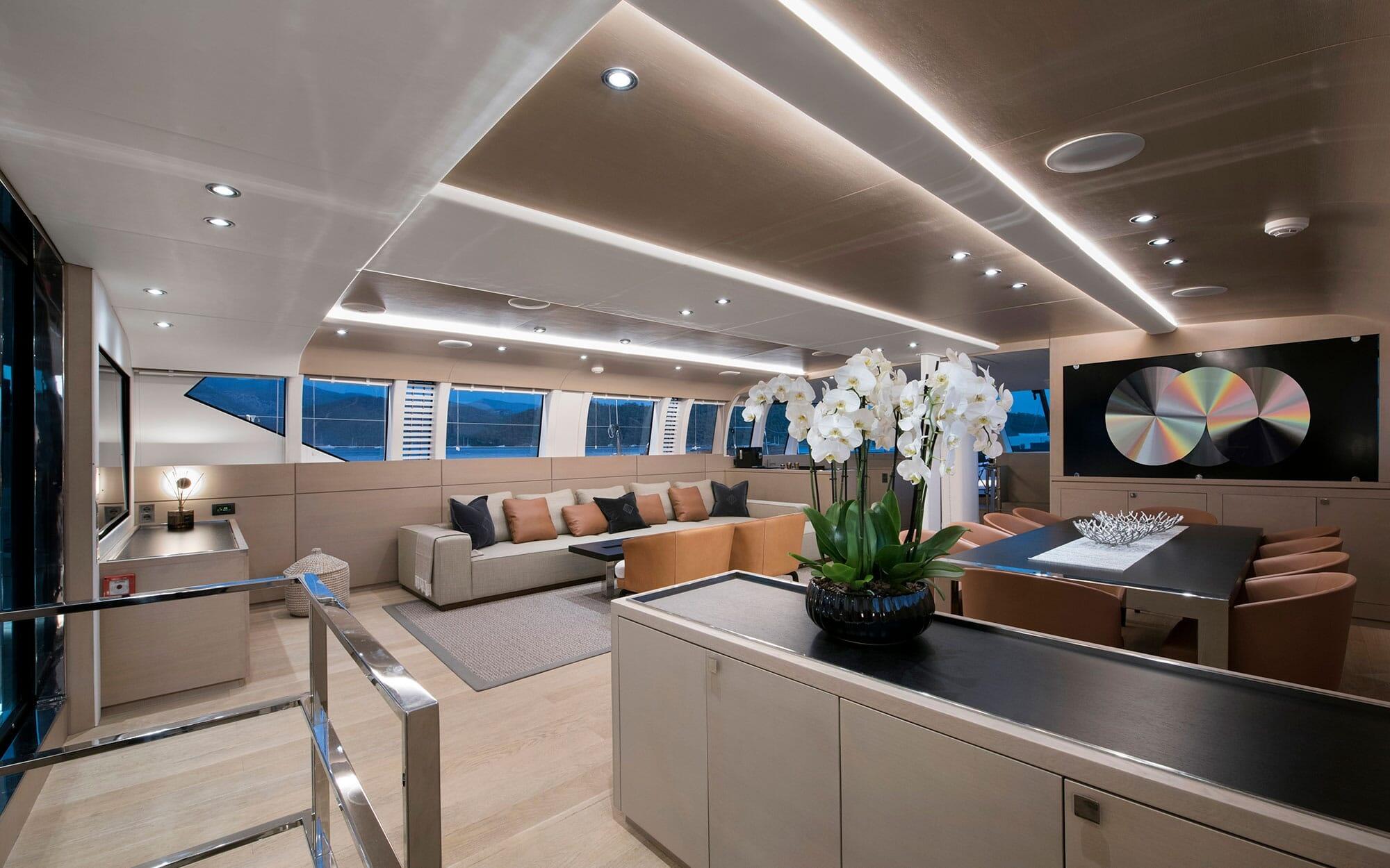 modern yacht main salon with L-shaped sofa, dining table, built-in cabinetry and panoramic windows