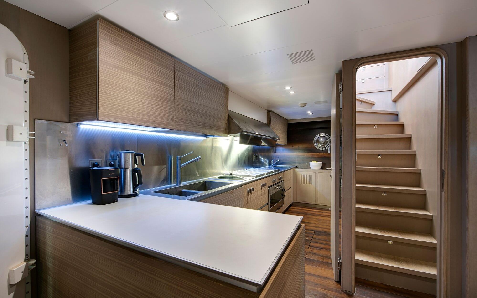 modern yacht galley kitchen with stainless steel appliances, LED lighting, and wooden stairs