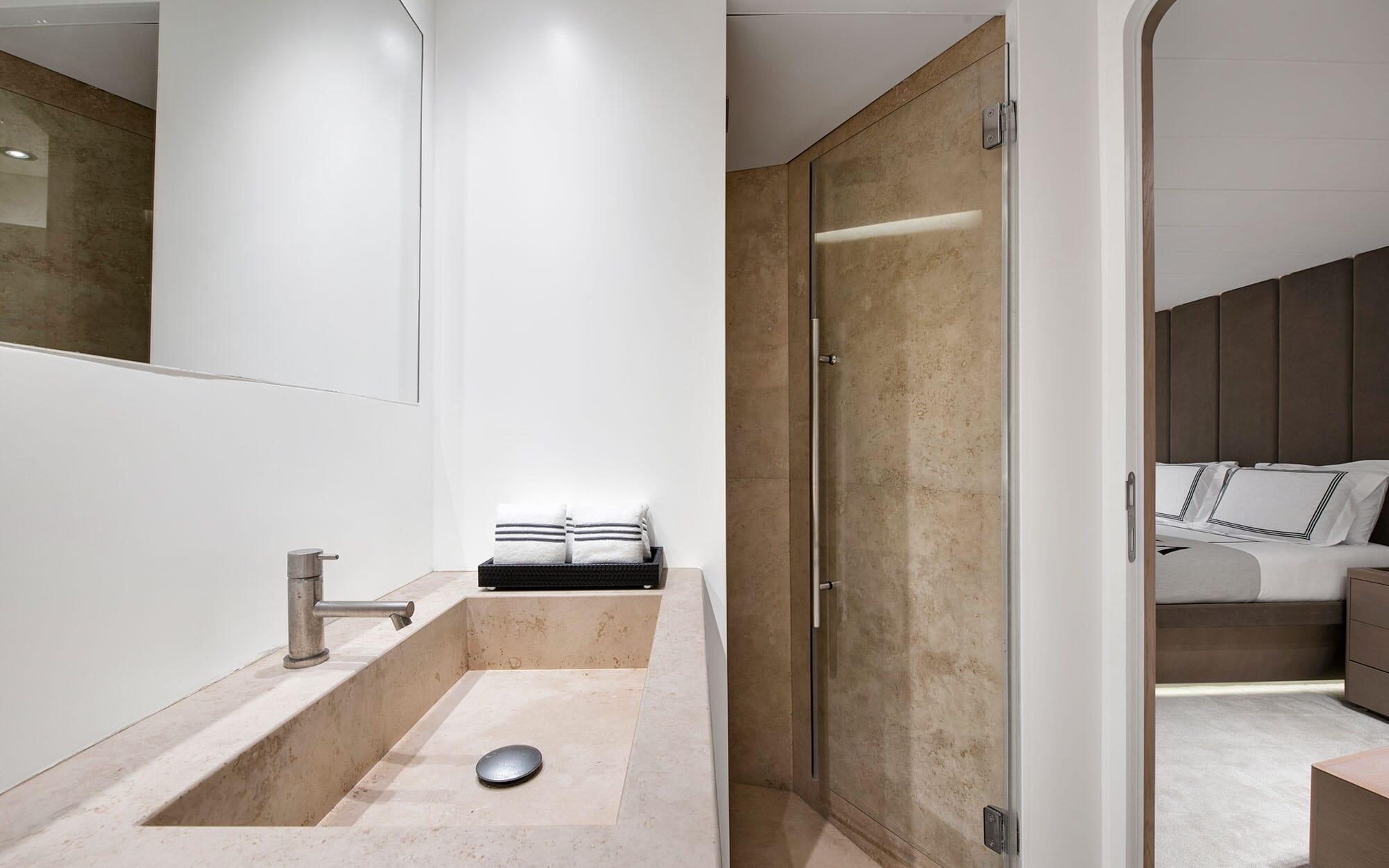 luxury yacht bathroom featuring beige stone sink, glass shower enclosure and bedroom view