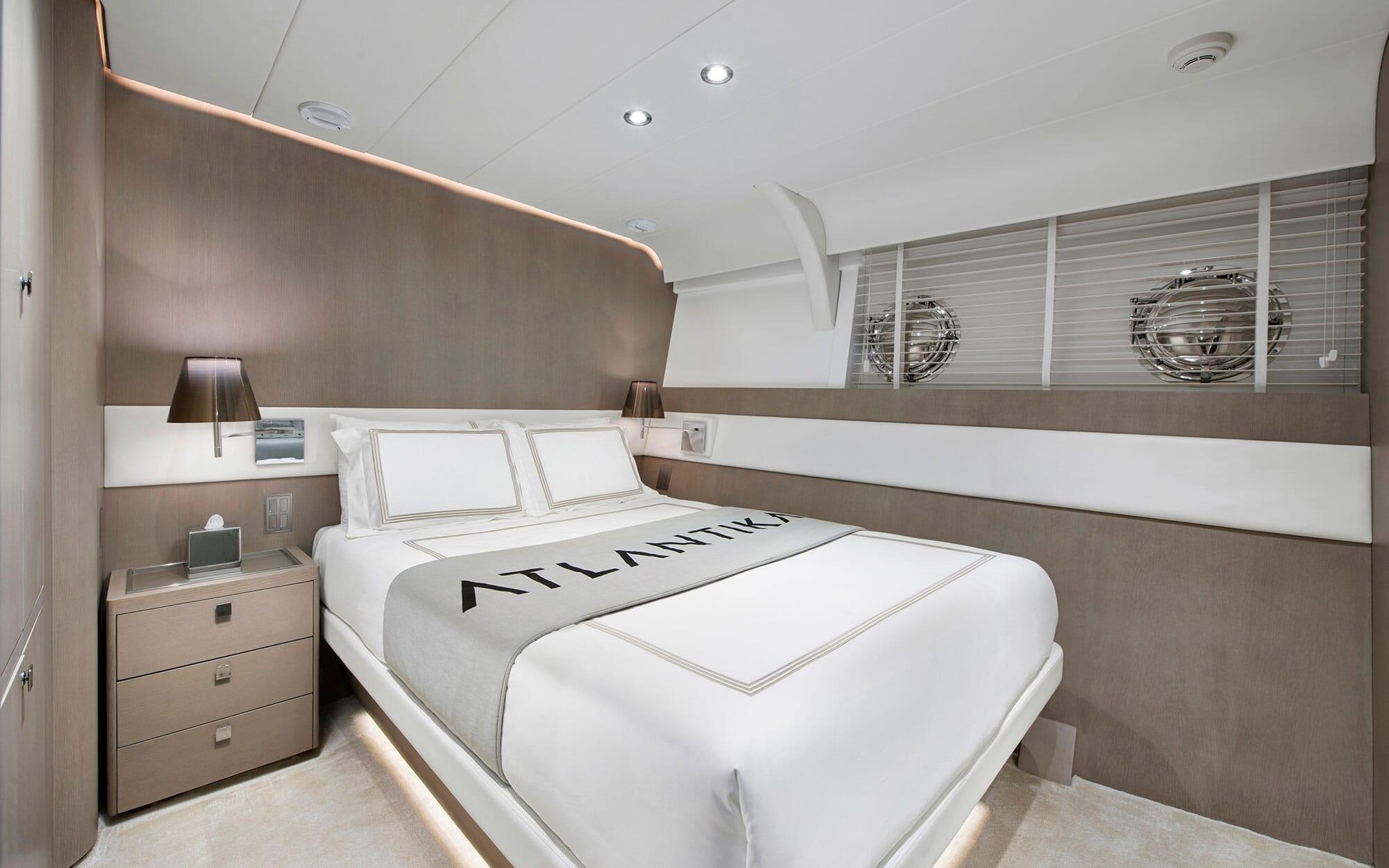 modern yacht cabin with double bed, white linens, bedside tables and portholes