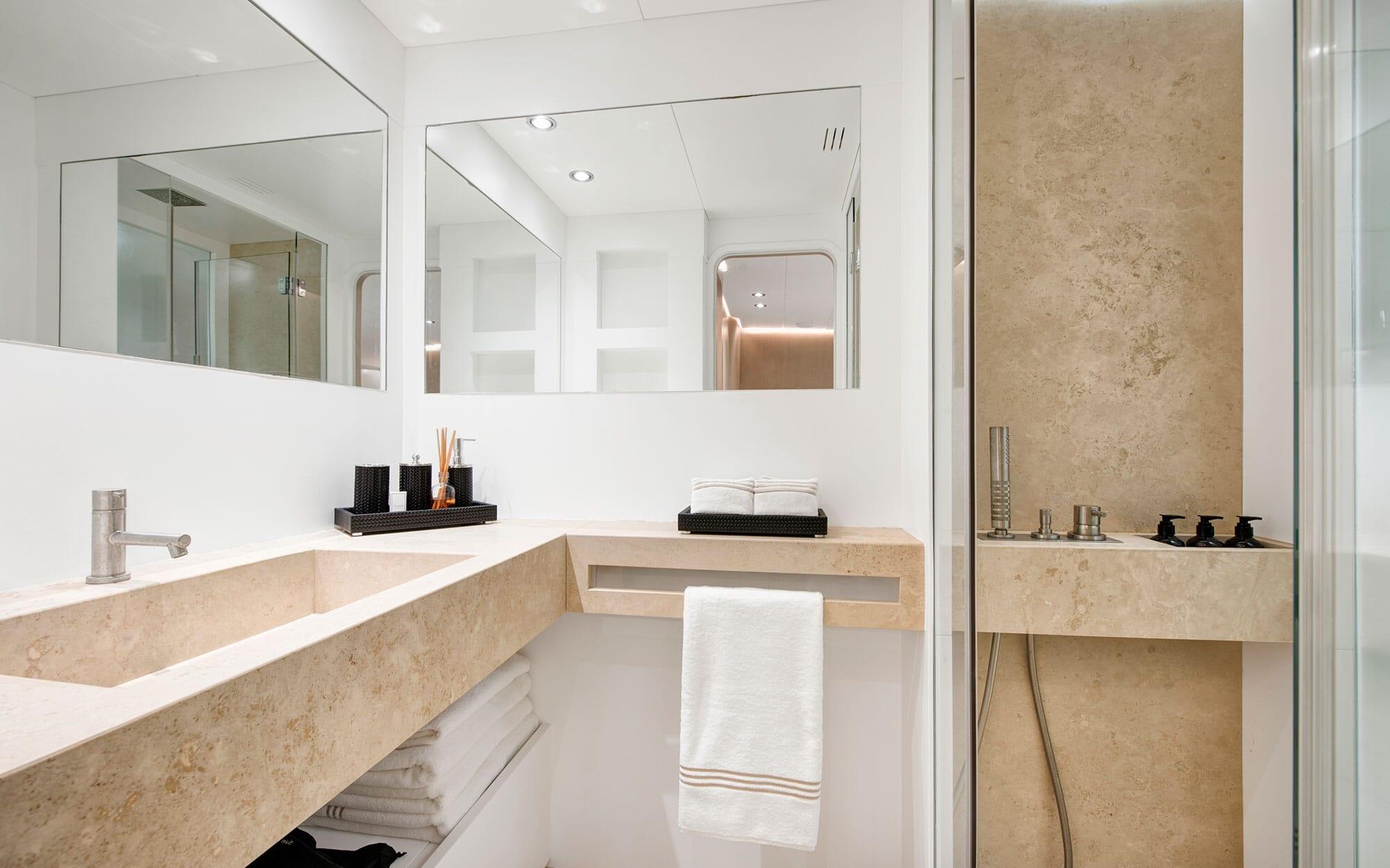 luxury yacht bathroom with beige marble vanity, dual mirrors, and glass shower enclosure